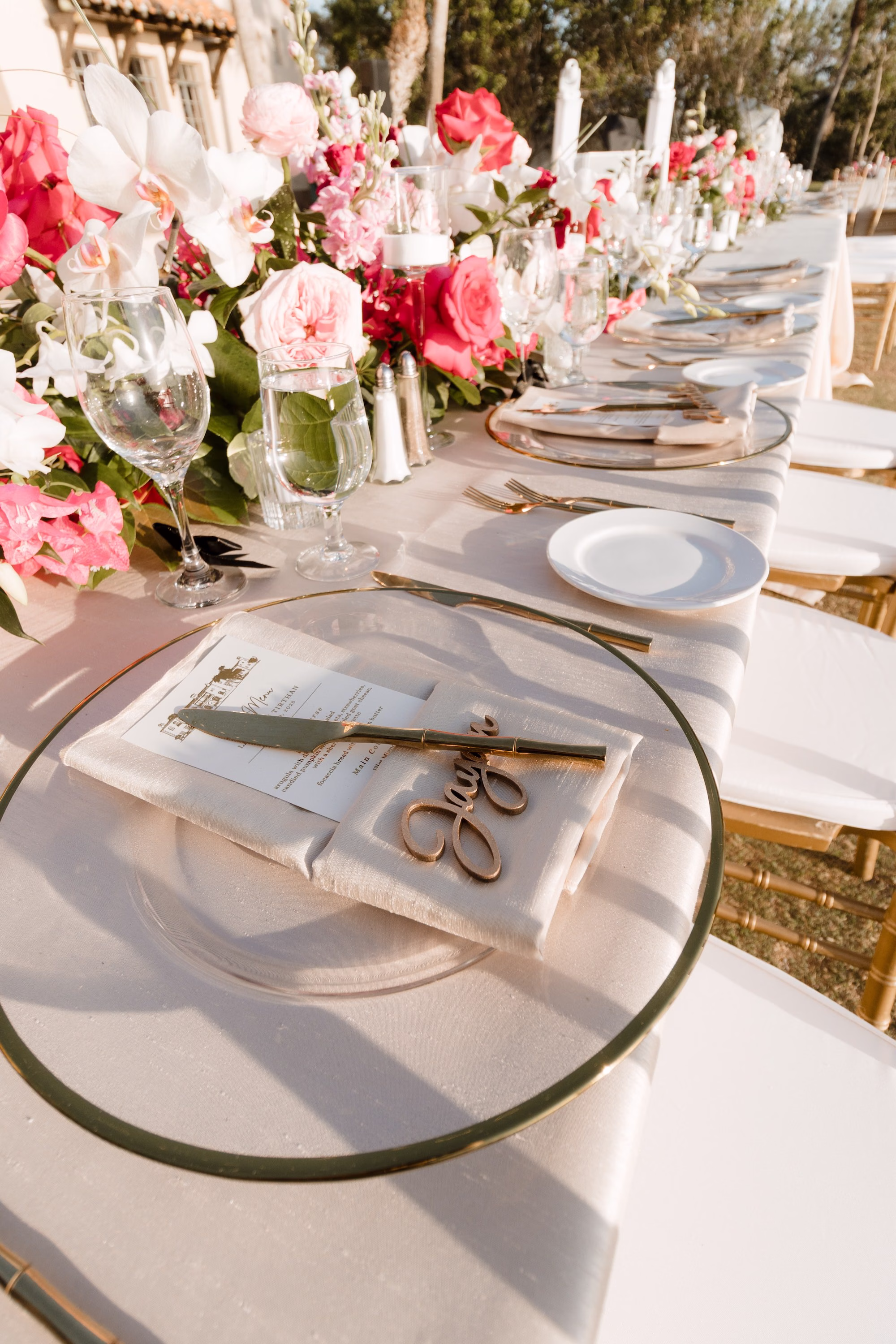 71Romantic Pink and Gold Waterfront Florida Wedding - Vibrant Pink and Gold Multicultural Sarasota Wedding | Powel Crosley Estate Garden Romantic Outdoor Wedding Reception | Gold Neutral Table Linens with Clear, Gold Rimmed Charger and Gold Cutlery Tablescape Decor Inspiration | White Rose with White Menu Card and Tan, Gold Napkin Reception Decor Ideas