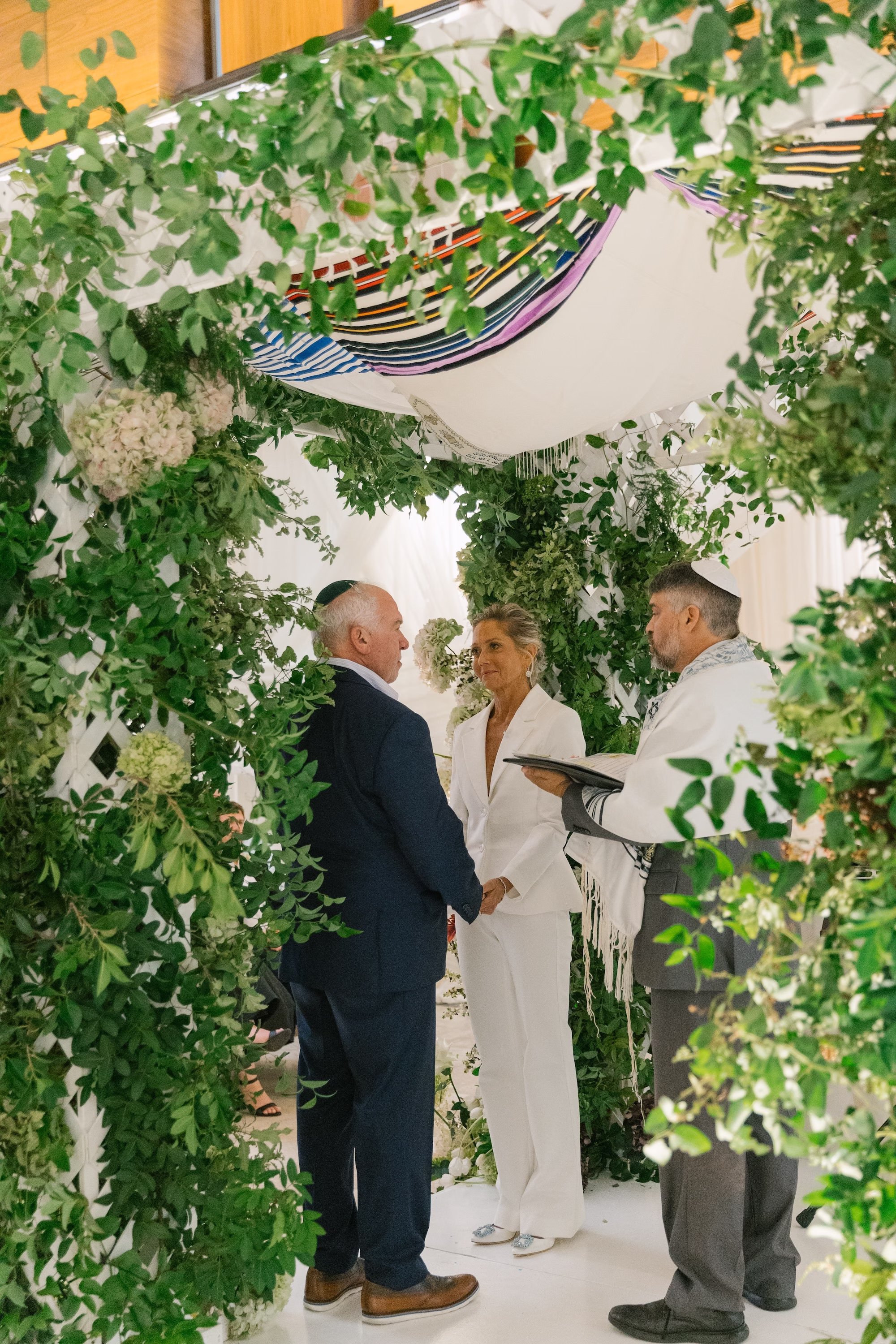 Bride and Groom Wedding Ceremony Vow Exchange Wedding Portrait | White Alice and Olivia Bridal Wedding Suit Inspiration | Traditional Jewish Wedding Chuppah of Lush Green Foliage and White Hydrangeas and Roses Ideas | St Pete Planner Stelloccasions Weddings and Events