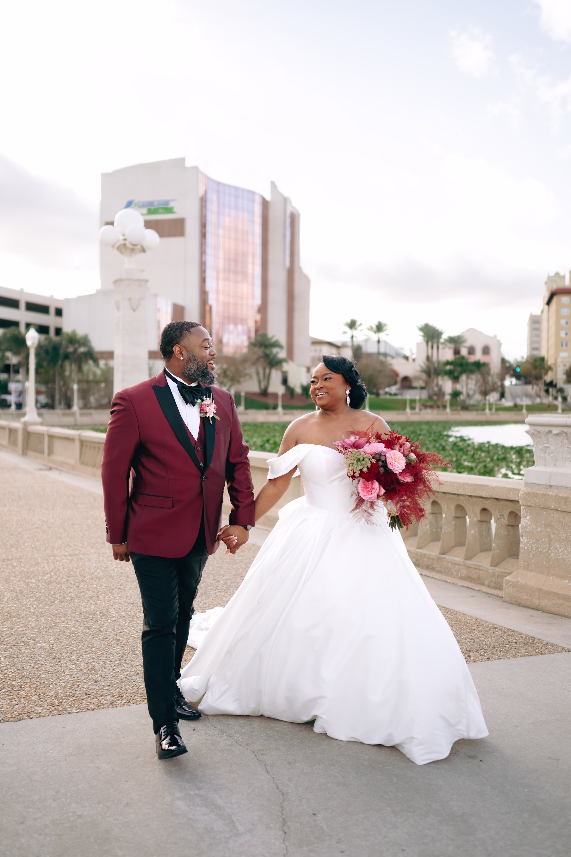 21Bold Pink Red and Burgundy Wedding Ideas Lakeland Wedding Venue Lake Mirror Amphitheater - Glamorous, Burgundy Lakeland Wedding | Lake Mirror Amphitheater Bride and Groom Wedding Portrait | Pink Roses with Red, Burgundy and Green Florals Bridal Wedding Bouquet Ideas | Off the Shoulder White Ball Gown Inspiration | Groom Red Suit Jacket Ideas | Lakeland Wedding Ceremony Venue Lake Mirror Amphitheater