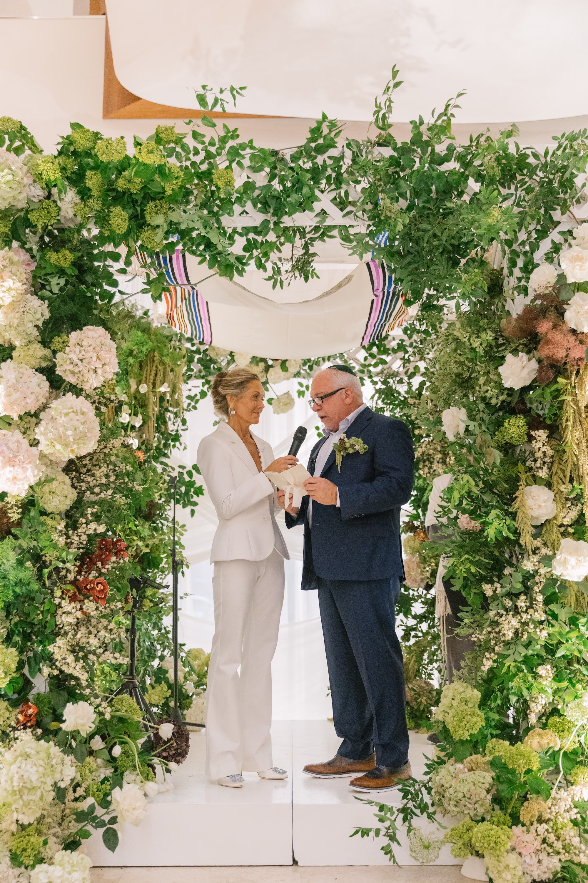 Bride and Groom Wedding Ceremony Vow Exchange Wedding Portrait | White Alice and Olivia Bridal Wedding Suit Inspiration | Traditional Jewish Wedding Chuppah of Lush Green Foliage and White Hydrangeas and Roses Ideas | St Pete Planner Stelloccasions Weddings and Events