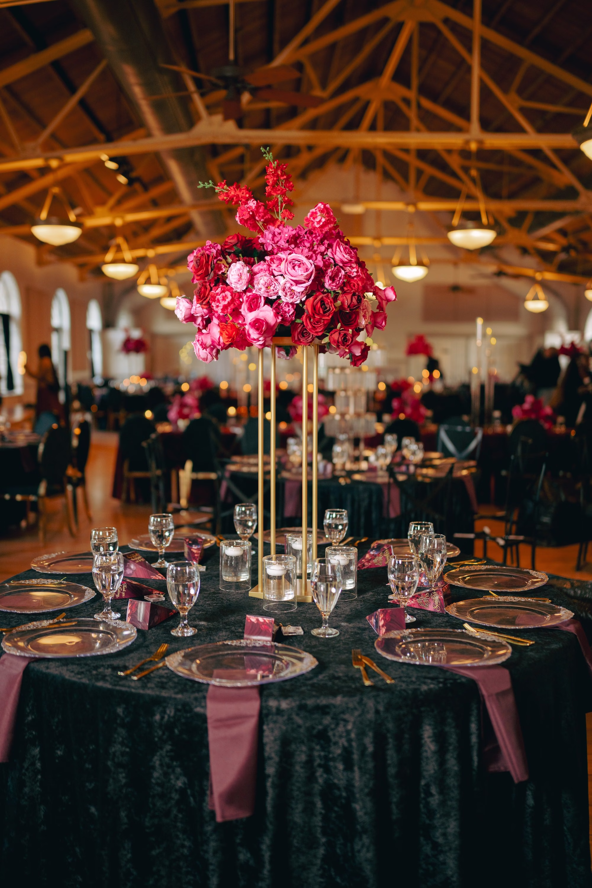 28Bold Pink Red and Burgundy Wedding Ideas - Glamorous, Burgundy Lakeland Wedding | Lake Mirror Amphitheater Glamourous Moody Red, Black, Pink and Burgundy Ballroom Wedding Reception Inspiration | Tall Gold Geometric Wedding Reception Centerpiece Flower Stand with Vibrant Pink, Deep Red, Dark Burgundy Roses Floral Arrangement Decor Ideas | Romantic Floating Tea Candles Reception Table Decor Inspiration | Clear Glass Chargers with Gold Rims on Black Table Linens Tablescape Decor Ideas