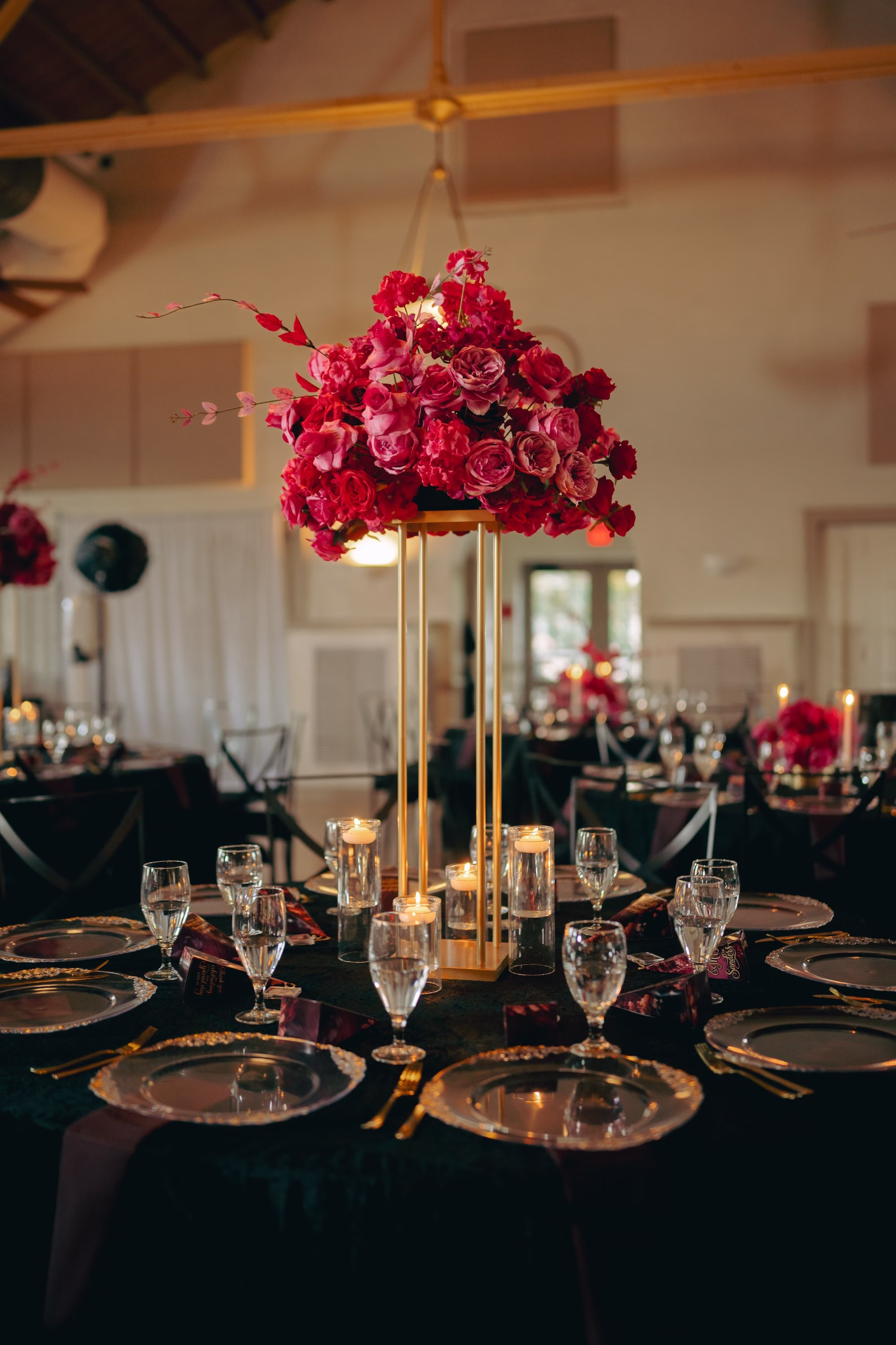 33Bold Pink Red and Burgundy Wedding Ideas - Glamorous, Burgundy Lakeland Wedding | Lake Mirror Amphitheater Glamourous Moody Red, Black, Pink and Burgundy Ballroom Wedding Reception Inspiration | Tall Gold Geometric Wedding Reception Centerpiece Flower Stand with Vibrant Pink, Deep Red, Dark Burgundy Roses Floral Arrangement Decor Ideas | Romantic Floating Tea Candles Reception Table Decor Inspiration | Clear Glass Chargers with Gold Rims on Black Table Linens Tablescape Decor Ideas
