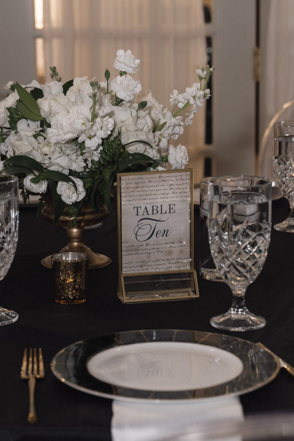 40Timeless Black and Wedding New Years Eve Wedding Ideas - Timeless Black and White Tarpon Springs Wedding | Whitehurst Gallery Timeless White and Black New Years Eve Ballroom Wedding Reception | Black Linens with Crystal Drinkware and Black and Gold Chargers with White Plate Tablescape Decor Inspiration | Elegant Black and White Table Number in Gold Frame Decor Tables Ideas | Monochromatic White Floral Centerpiece in Gold Vase Inspiration