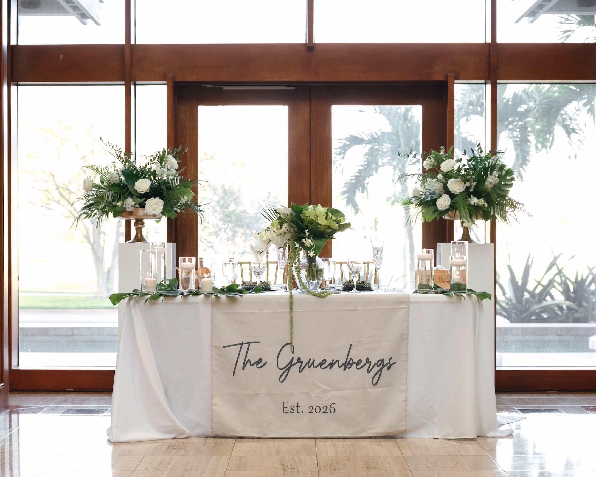 40Tropical Green Florida Wedding Ideas - Tropical, Green Downtown St. Pete Wedding | Poynter Institute Tropical Green and White Luxurious Ballroom Wedding Reception Sweetheart Table | Modern Gold Chiavari Chairs | Tall Gold Vase Centerpieces with White Florals and Greenery Arrangement Ideas | White Linens with New Last Name Runner Tablescape Decor Inspiration | St Pete Event Planner Coastal Coordinating | Florida Venue Poynter Institute