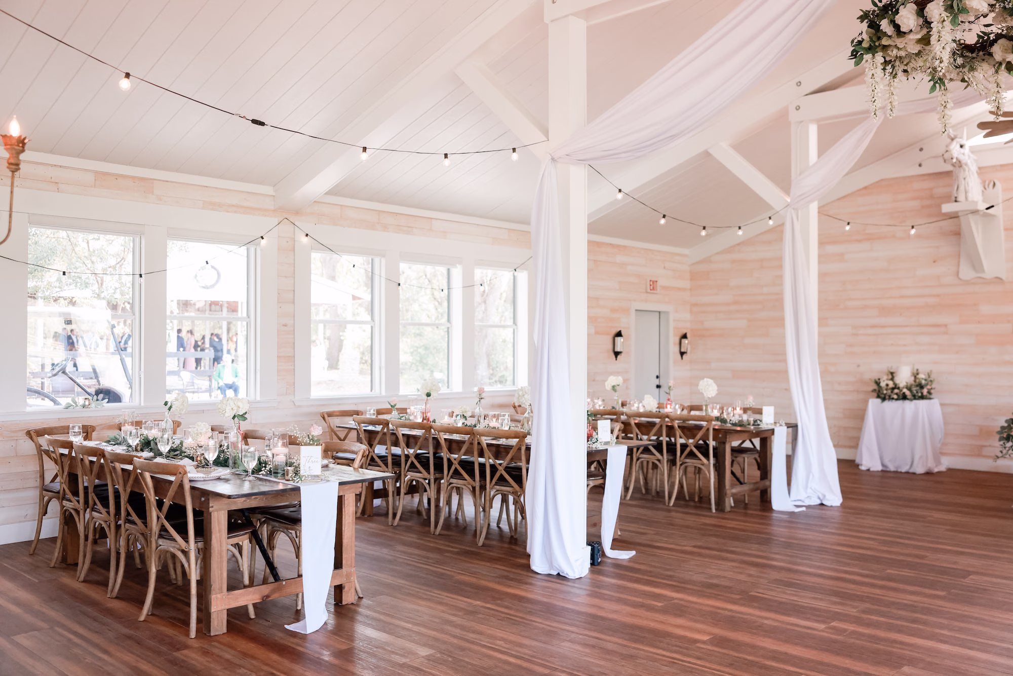 Rustic Elegant White and Green Spring Wedding Wedding Reception Decor Inspiration | Long Wooden Feasting Tables with Greenery Garland Tablescape Decor Ideas | White Draping and Romantic String Lighting Decor Inspiration | Tampa Bay Event Venue Legacy Lane Weddings