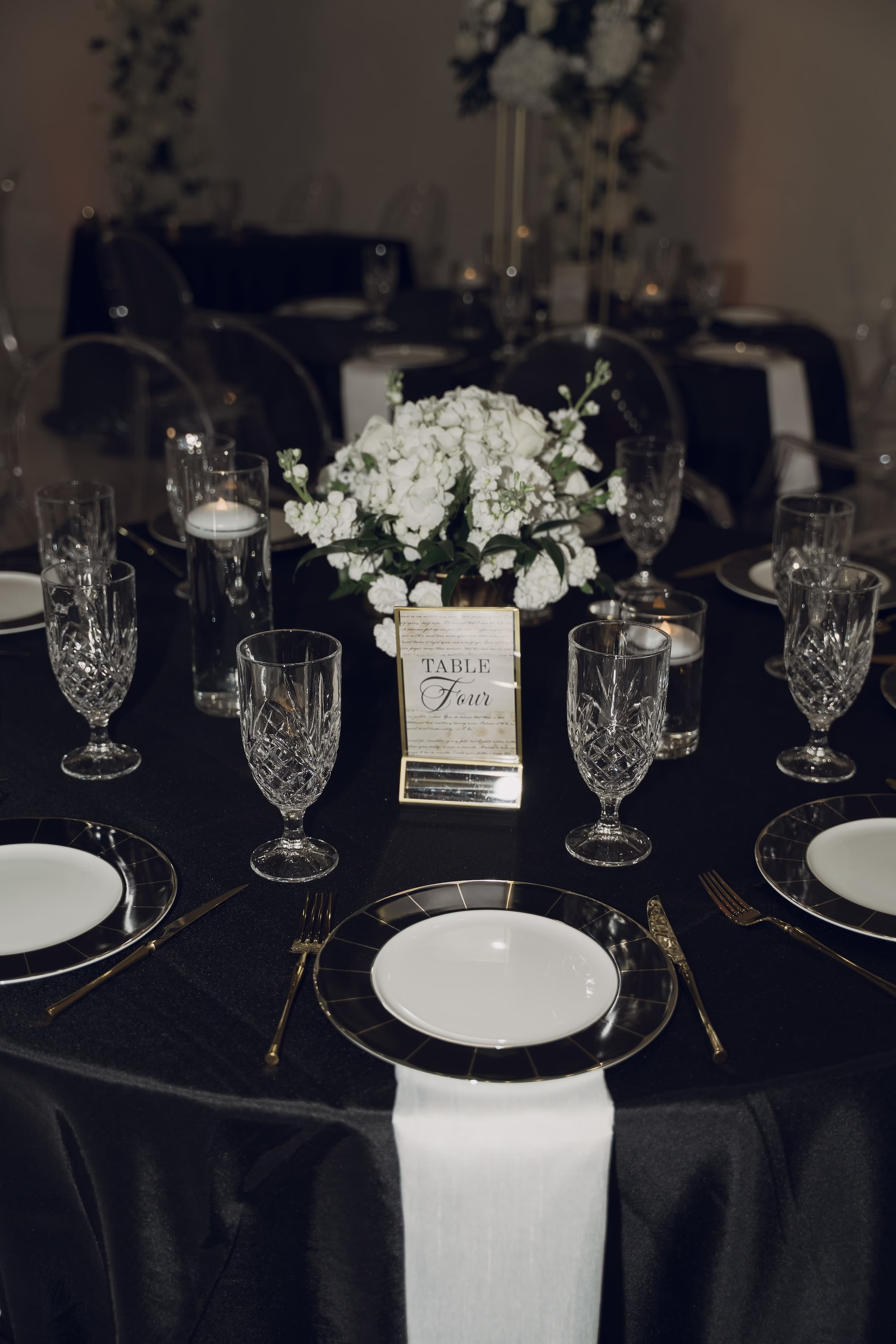 42Timeless Black and Wedding New Years Eve Wedding Ideas - Timeless Black and White Tarpon Springs Wedding | Whitehurst Gallery Timeless White and Black New Years Eve Ballroom Wedding Reception | Black Linens with Crystal Drinkware and Black and Gold Chargers with White Plate Tablescape Decor Inspiration | Monochromatic White Floral Centerpiece with Floating Tea Candles Decor Ideas