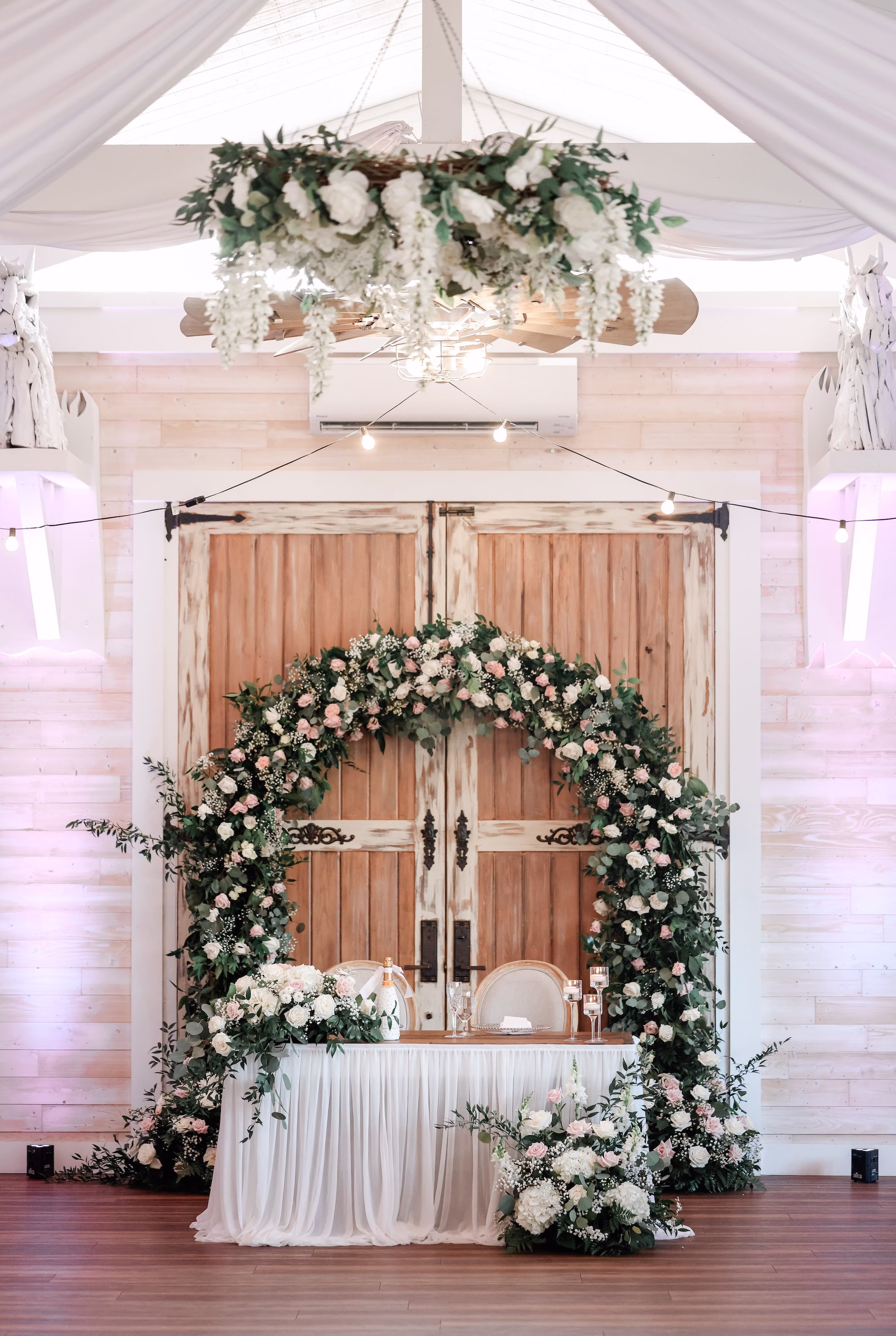 Romantic Chic Sweetheart Table with Rustic Barn Doors and Whimsical Blush and White Floral Arch Wedding Reception Decor Inspiration | Overhead Ceiling Wreath of Eucalyptus and White Hydrangeas Hanging Decor Ideas | Tampa Bay Event Venue Legacy Lane Weddings