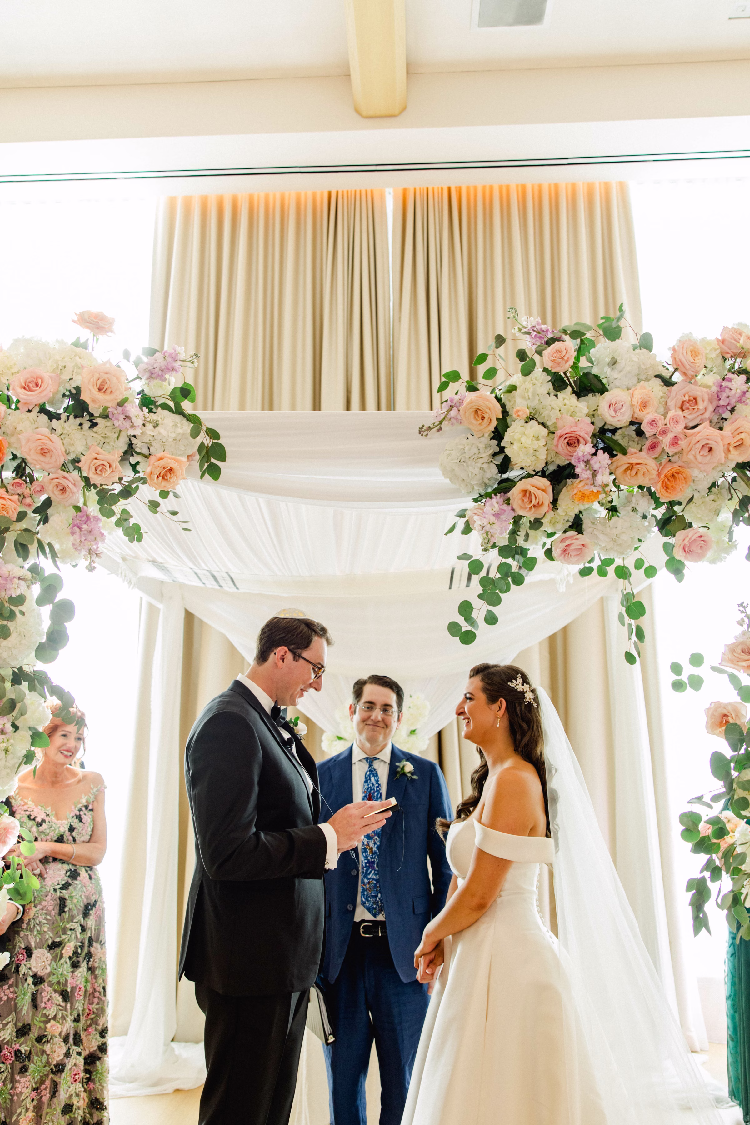 Bride and Groom Wedding Ceremony Vow Exchange Wedding Portrait | Spring Pastel Roses, Hydrangeas Blush, Peach, Cream, White Wedding Ceremony Floral Arrangement Decor Inspiration | White Draping and Spring Floral Decor on Wedding Chuppah Jewish Wedding Ceremony Decor Ideas | Downtown Event Venue The Edition Hotel Tampa