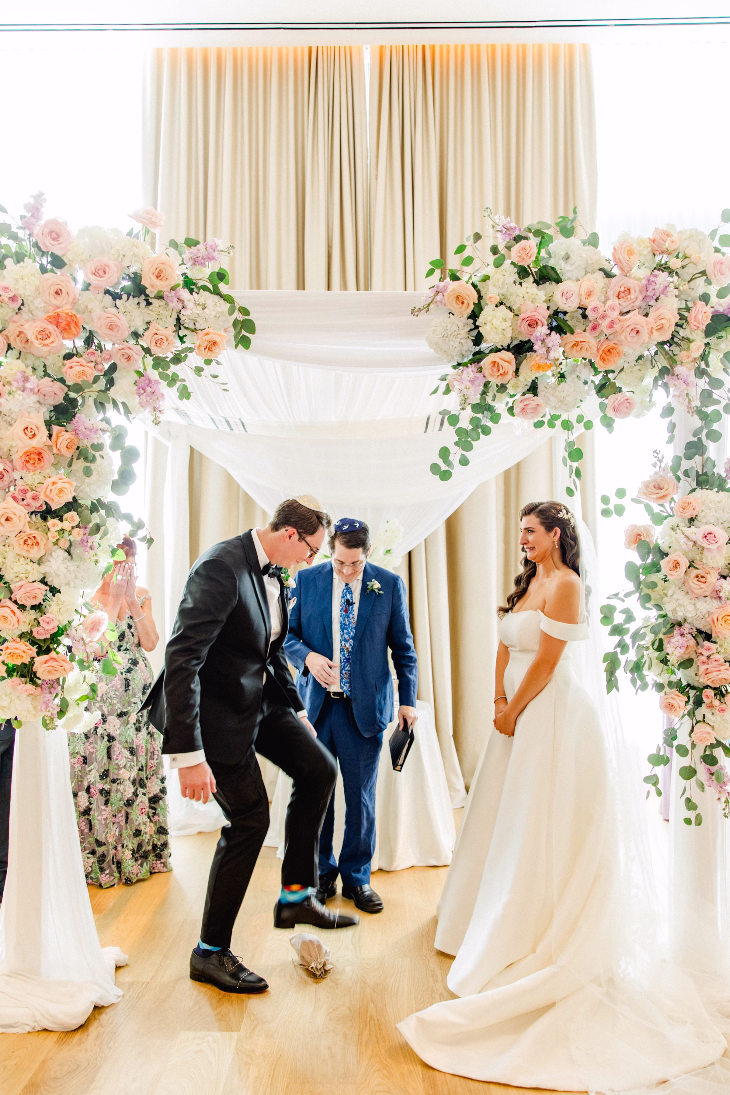 Bride and Groom Breaking Glass Jewish Wedding Ceremony Tradition Wedding Portrait | Spring Pastel Roses, Hydrangeas Blush, Peach, Cream, White Wedding Ceremony Floral Arrangement Decor Inspiration | White Draping and Spring Floral Decor on Wedding Chuppah Jewish Wedding Ceremony Decor Ideas