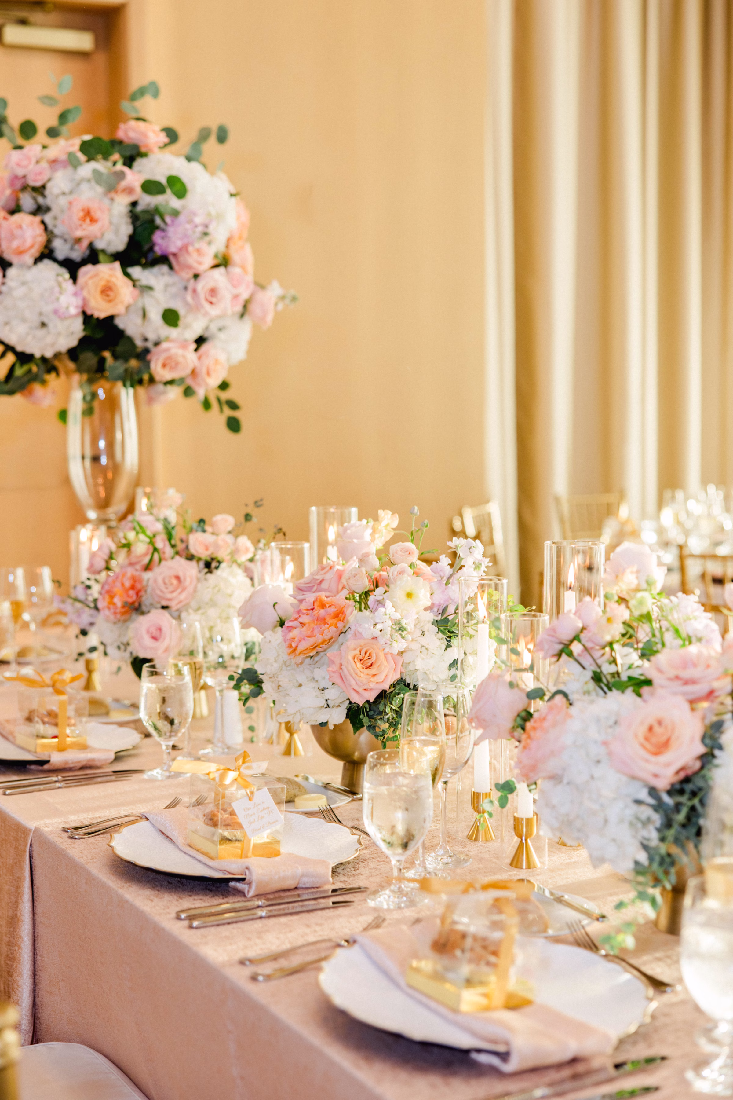 Luxurious Ballroom Wedding Reception | Tall Centerpieces with Pastel Pink, White Hydrangeas and Roses in Greenery Eucalyptus Flower Arrangement Centerpiece Ideas | Blush, Peach, Ivory Tablescape with Gold Accents Reception Decor Inspiration | White Charger with Champagne Blush Satin Napkin and Crystal Glasses Tablescape Decor Ideas