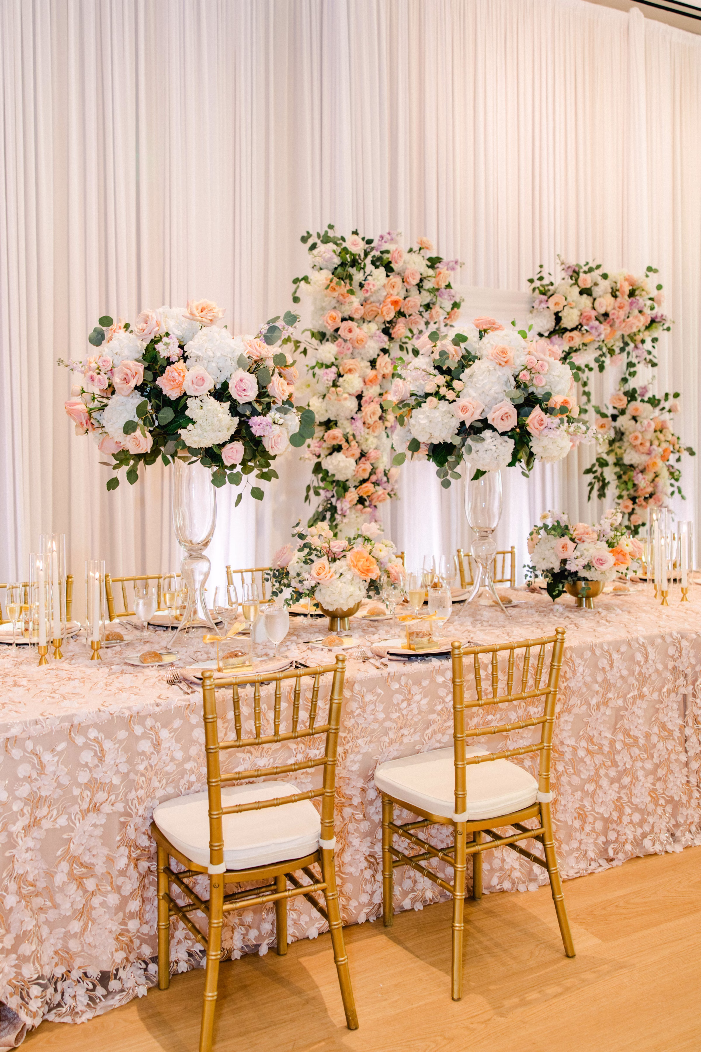 Spring Pastel Roses, Hydrangeas Blush, Peach, Cream, White Wedding Reception Floral Arrangement Centerpiece Decor Inspiration | Gold Chiavari Wedding Reception Chairs Ideas | Long Feasting Table with Blush Floral Table Linens Decor Inspiration
