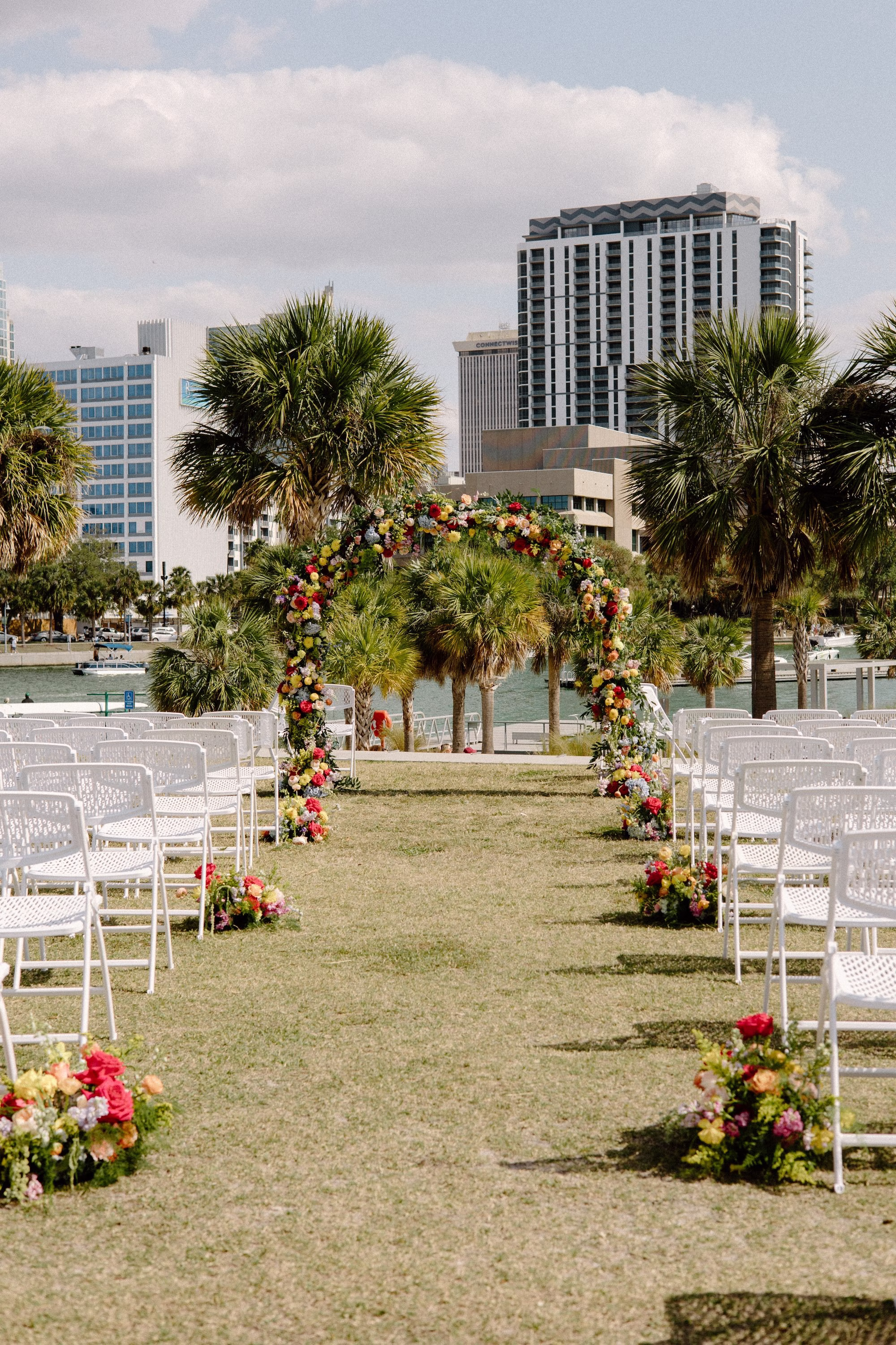 23Whimsical Pastel Spring Orange Yellow and Purple Wedding Inspiration - Whimsical, Colorful Waterfront Wedding | Tampa River Center Colorful Spring Garden Riverfront Wedding Ceremony Inspiration | White Garden Ceremony Chairs | Rounded Floral Wedding Ceremony Altar Arch with Spring Pastel Orange, Yellow, Lavender, Blush Floral Ideas | Floral Arrangement Aisle Decor Inspiration | Planner Wilder Mind Events | Venue Tampa River Center