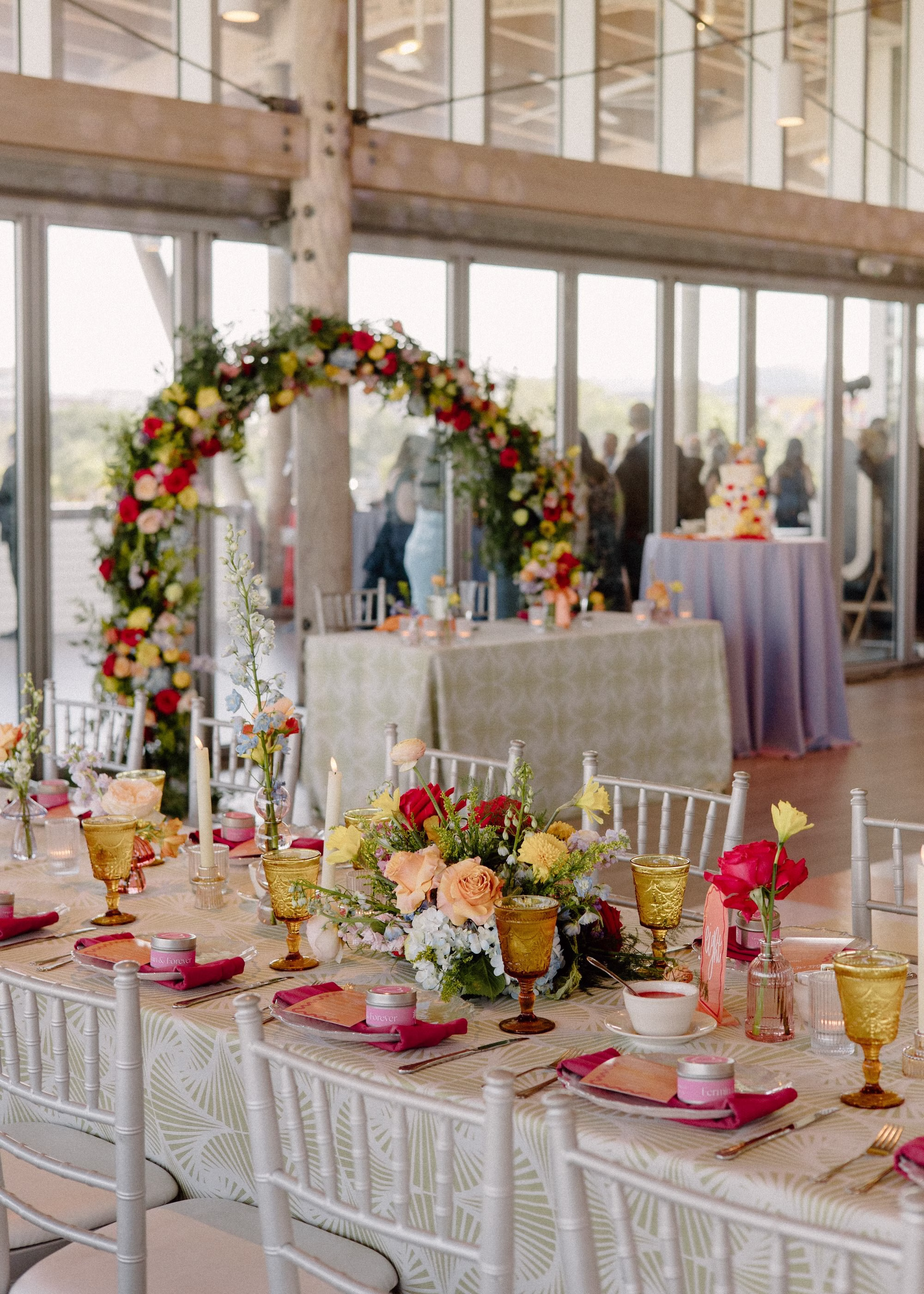 35Whimsical Pastel Spring Orange Yellow and Purple Wedding Inspiration - Whimsical, Colorful Waterfront Wedding | Tampa River Center Rounded Floral Wedding Reception Sweetheart Table Decor Arch with Spring Pastel Orange, Yellow, Lavender, Blush Floral Ideas | White Chiavari Chairs with Textured Linens Decor Inspiration | Colored Depression Glassware with Bright Pink Napkins Tablescape Reception Decor Ideas | Planner Wilder Mind Events