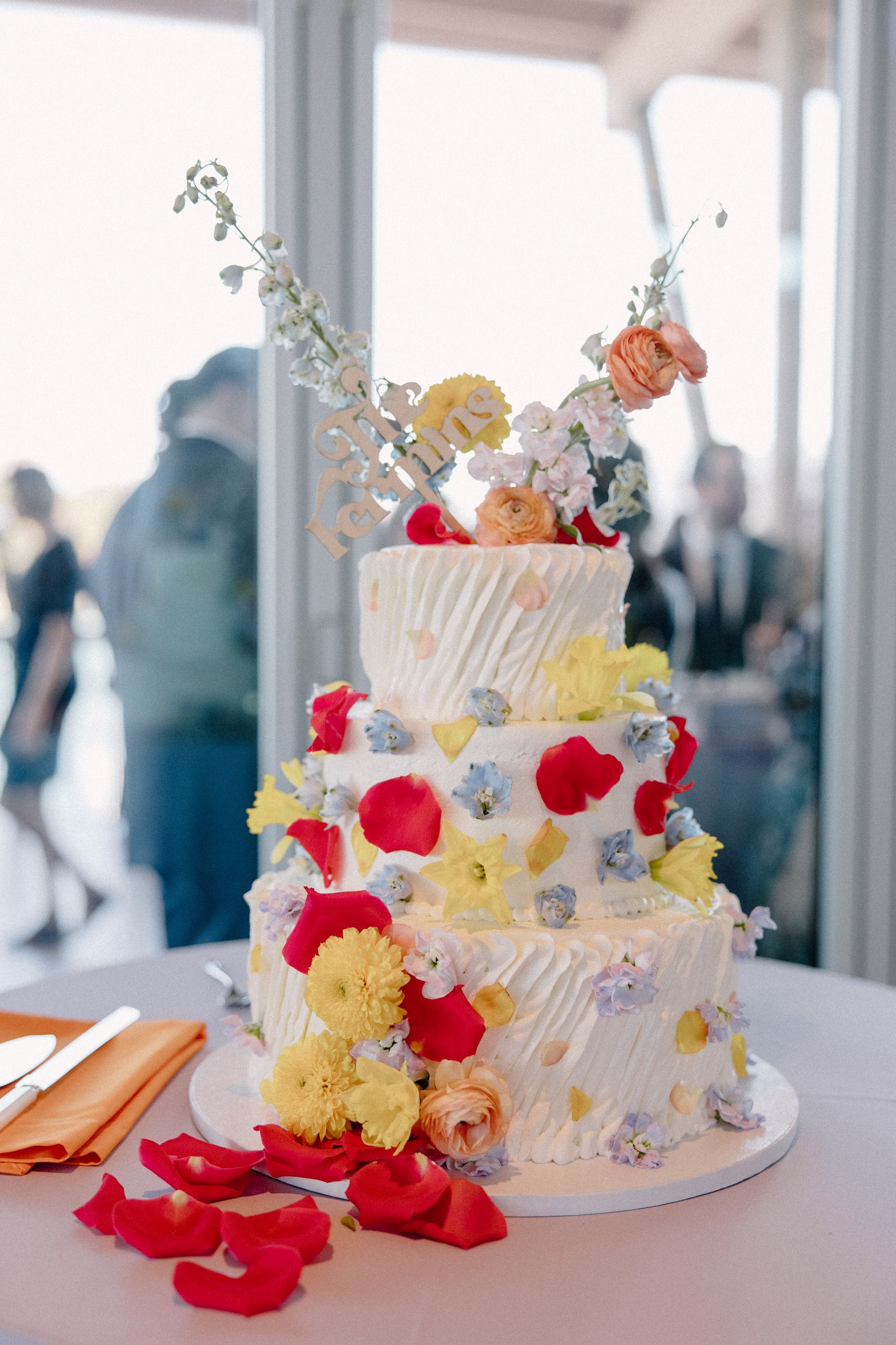 50Whimsical Pastel Spring Orange Yellow and Purple Wedding Inspiration - Whimsical, Colorful Waterfront Wedding | Tampa River Center Three Tier White Wedding Cake with Red, Baby Blue, Pastel Yellow Floral Decor Inspiration
