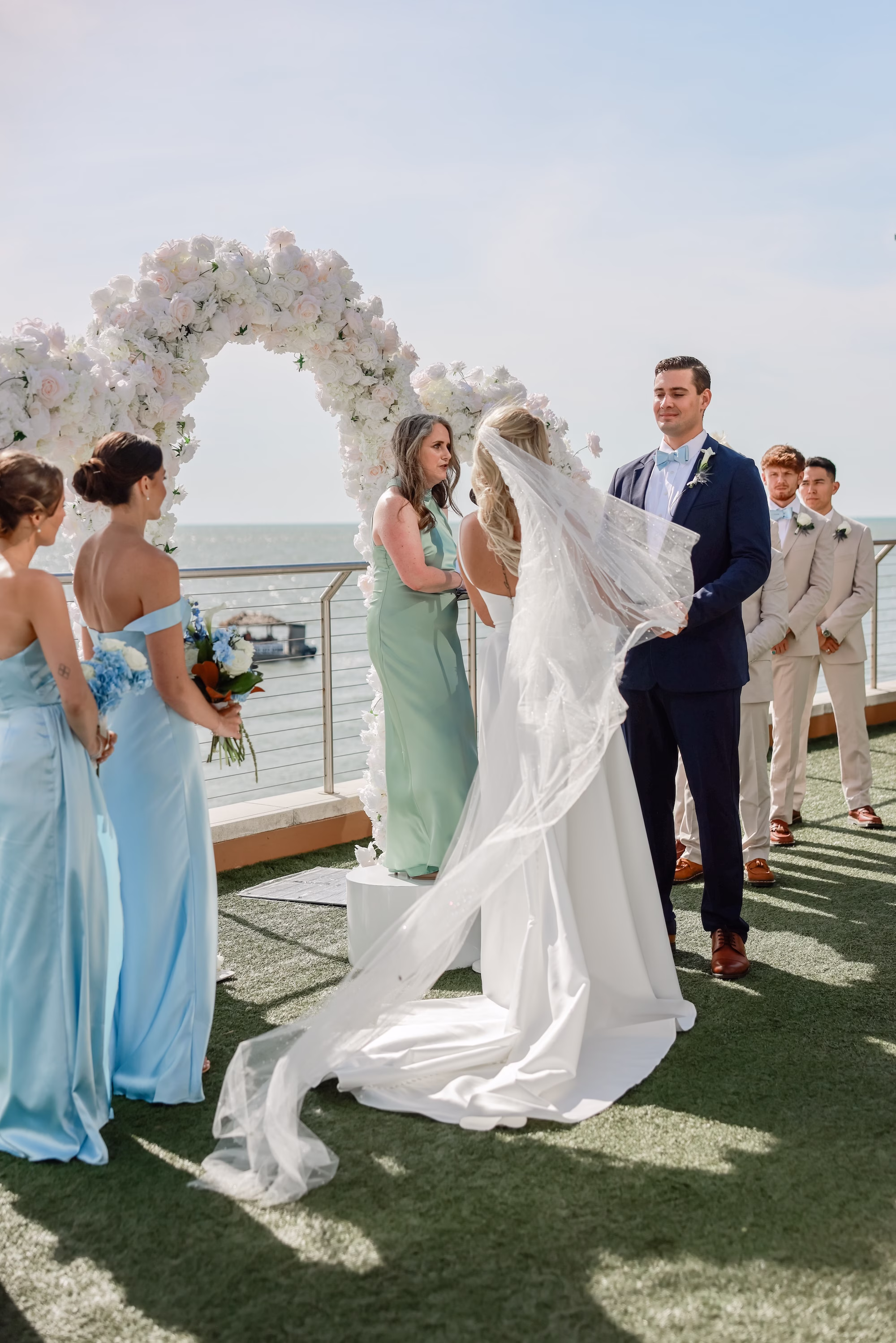 20Elegant Light Blue Coastal Florida Wedding Ideas - Elegant Blue Modern Coastal Wedding | Opal Sands Clearwater Beach Bride in Cathedral Veil and Groom at White Floral Arch Rooftop Wedding Ceremony Portrait with Bridesmaids in Light Blue Dresses