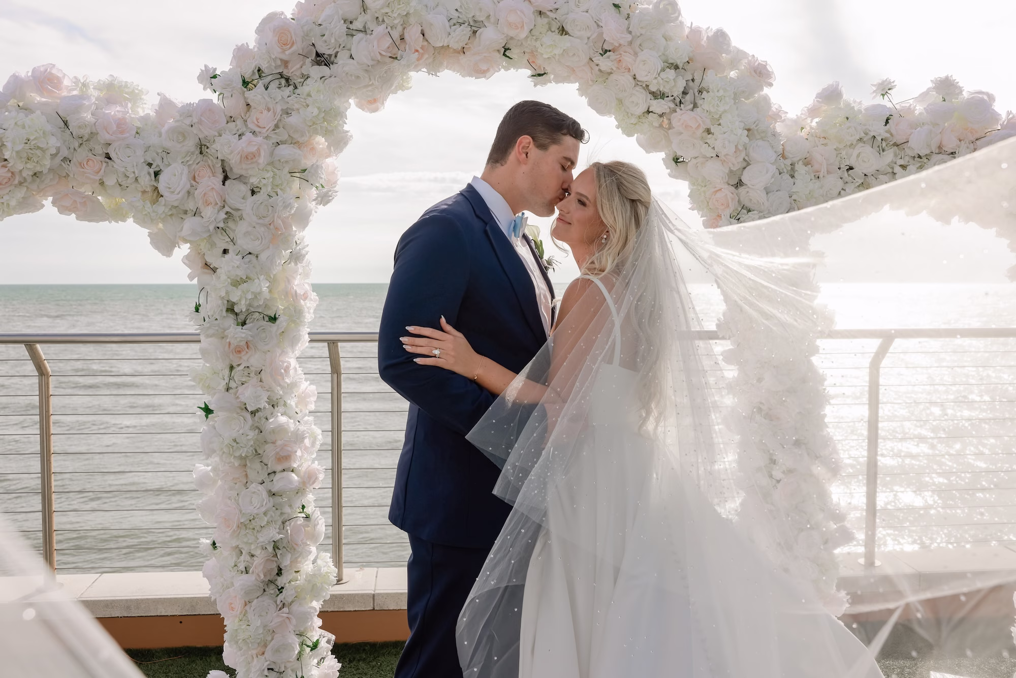 24Elegant Light Blue Coastal Florida Wedding Ideas - Elegant Blue Modern Coastal Wedding | Opal Sands Clearwater Beach Bride and Groom Forehead Touch Wedding Portrait Under White Floral Arch with Flowing Cathedral Veil | Tampa Bay Photography Lifelong Photography Studio
