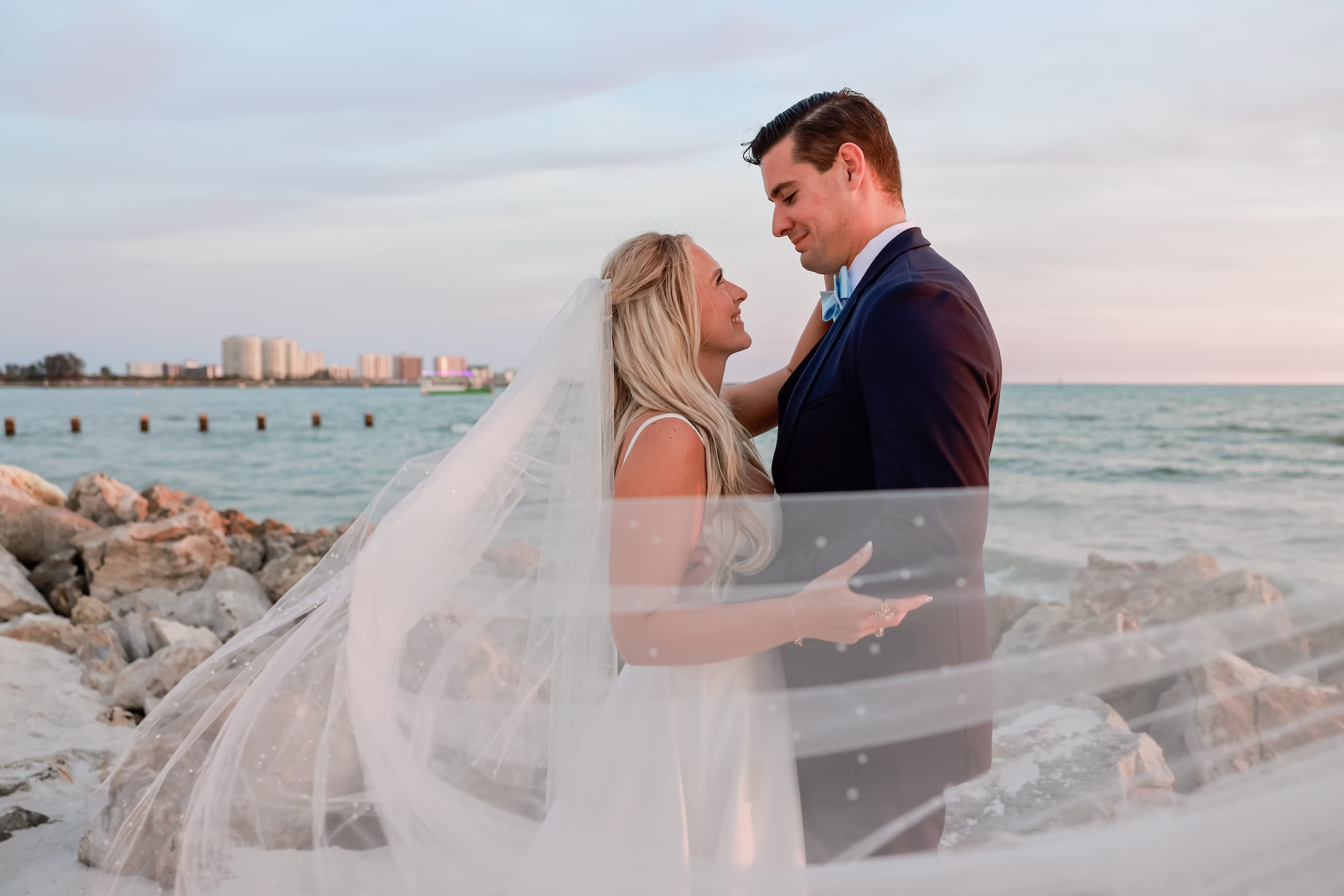 28Elegant Light Blue Coastal Florida Wedding Ideas Clearwater Venue Opal Sands - Elegant Blue Modern Coastal Wedding | Opal Sands Clearwater Beach Bride and Groom Sunset Wedding Portrait on Rock Jetty with Cathedral Veil Blowing in the Wind and Clearwater Beach Skyline | Tampa Bay Photography Lifelong Photography Studio | Venue Opal Sands Resort