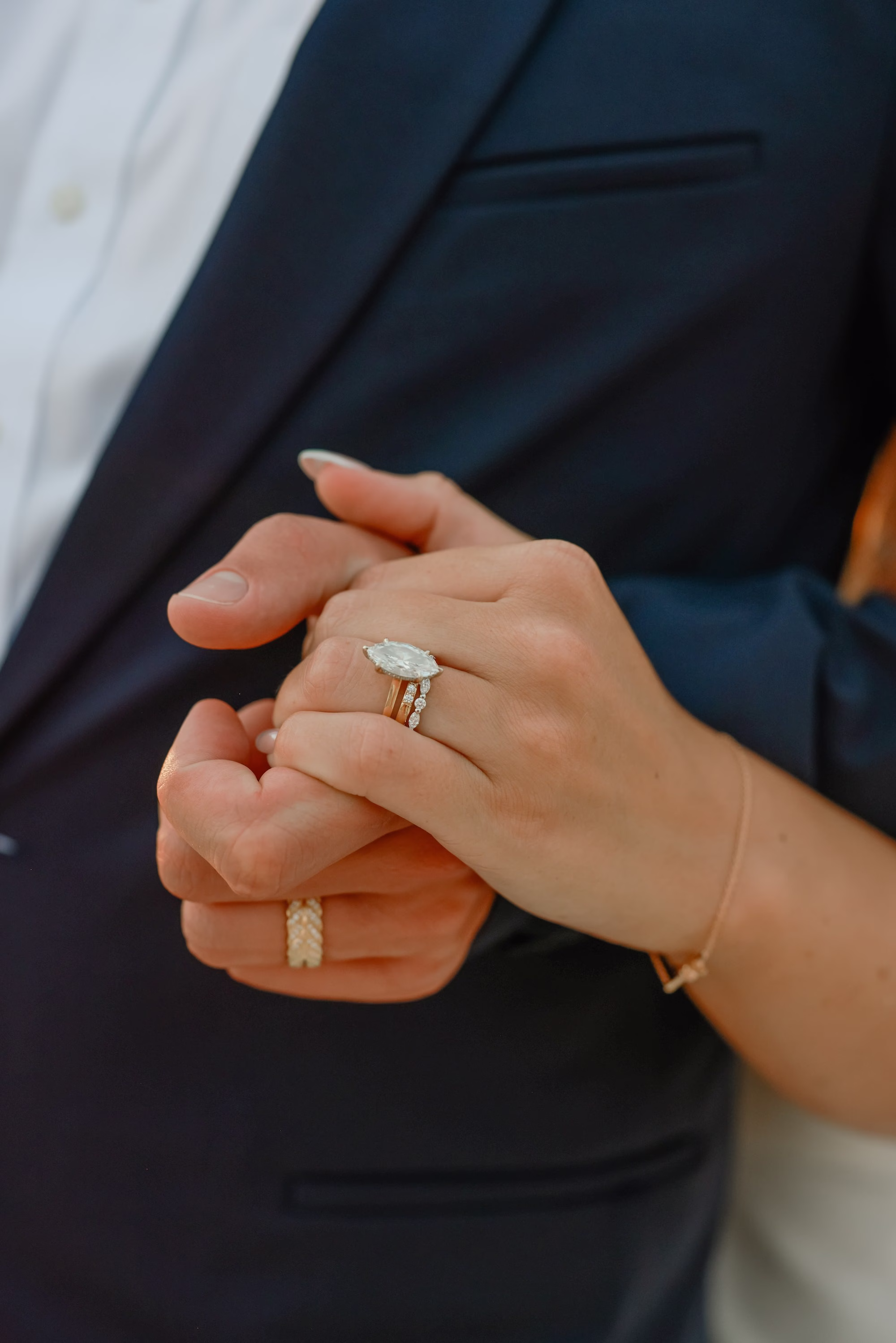 31Elegant Light Blue Coastal Florida Wedding Ideas - Elegant Blue Modern Coastal Wedding | Opal Sands Clearwater Beach Close-Up of Bride's Oval Diamond Engagement Ring and Wedding Band Holding Groom's Hand on Navy Suit