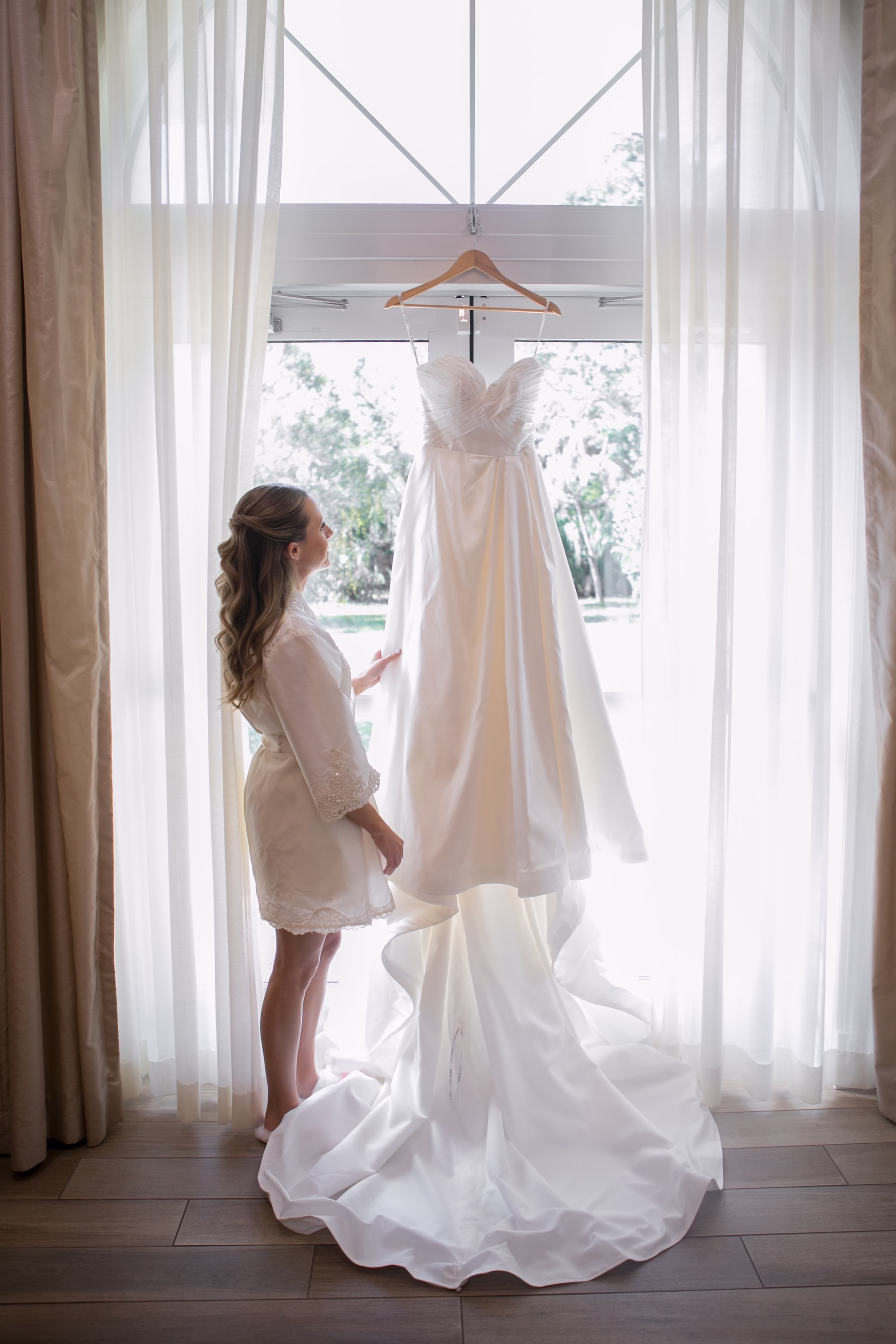 3Classic Black and White Wedding Ideas - Classic Black and White Clearwater Wedding | Harborside Chapel & The Fenway Bride Getting Ready Wedding Portrait | Strapless White Sweetheart Neckline Wedding Gown with Long Train hanging in Front of Bay Window Inspiration | Half Up Half Down Curled Bridal Wedding Hair Ideas | Tampa Bay Photographer Carrie Wildes Photography Art and Design | Clearwater Hair and Makeup Artist Femme Akoi Beauty Studio