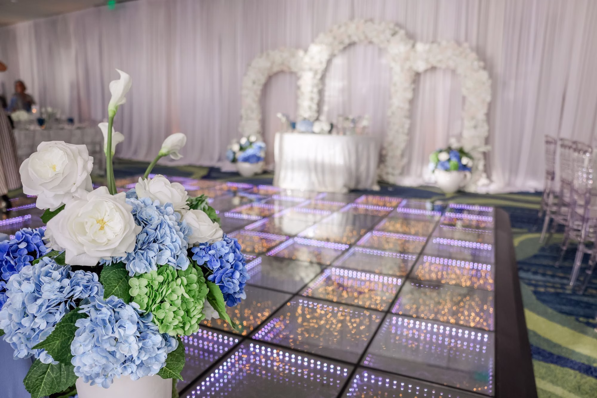40Elegant Light Blue Coastal Florida Wedding Ideas - Elegant Blue Modern Coastal Wedding | Opal Sands Clearwater Beach White Floral Arch Sweetheart Table Backdrop with LED Infinity Dance Floor and Blue Hydrangea Arrangement Wedding Reception Decor Ideas | Clearwater Beach Venue Opal Sands Resort | Gabro Event Rentals