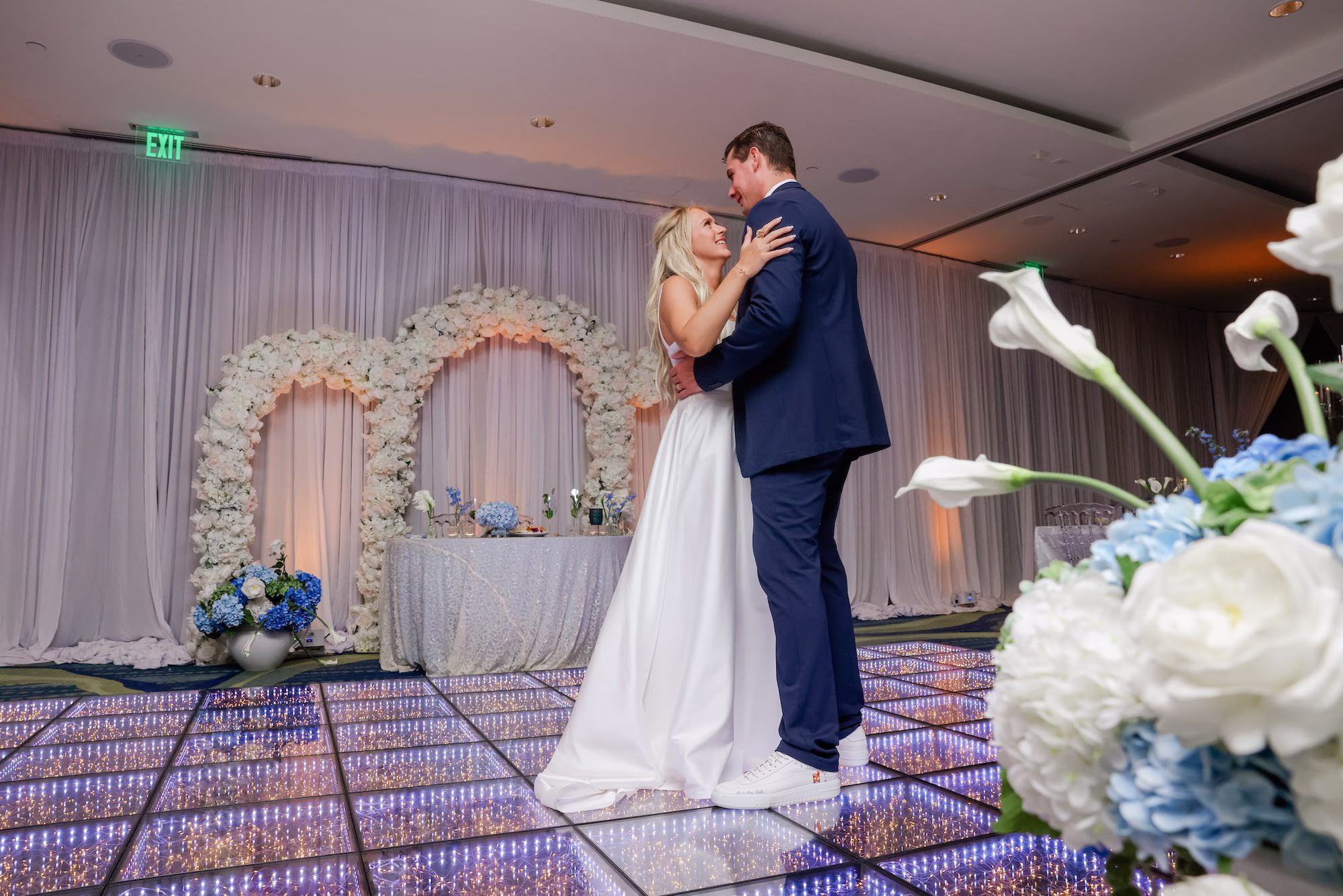 46Elegant Light Blue Coastal Florida Wedding Ideas Elegant Light Blue Coastal Florida Wedding Ideas Clearwater Venue Opal Sands - Elegant Blue Modern Coastal Wedding | Opal Sands Clearwater Beach Bride and Groom First Dance Wedding Portrait on LED Infinity Dance Floor in Front of White Floral Arch | Clearwater Beach Venue Opal Sands Resort | DJ Grant Hemond & Associates