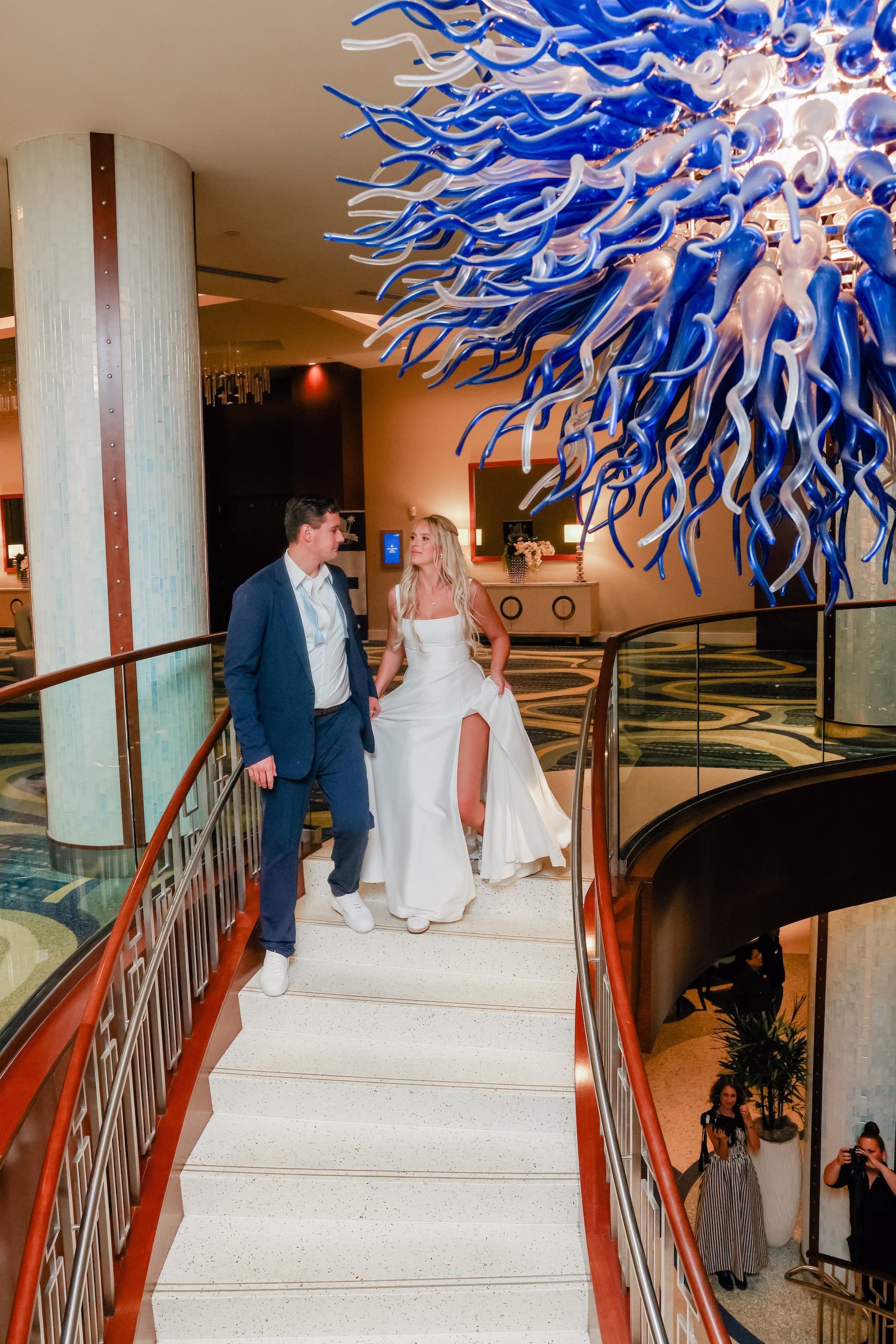 49Elegant Light Blue Coastal Florida Wedding Ideas Elegant Light Blue Coastal Florida Wedding Ideas Clearwater Venue Opal Sands - Elegant Blue Modern Coastal Wedding | Opal Sands Clearwater Beach Bride and Groom Walking Down Resort Staircase Under Blue Glass Chandelier Wedding Portrait | Clearwater Beach Venue Opal Sands Resort | Photography Lifelong Photography Studio