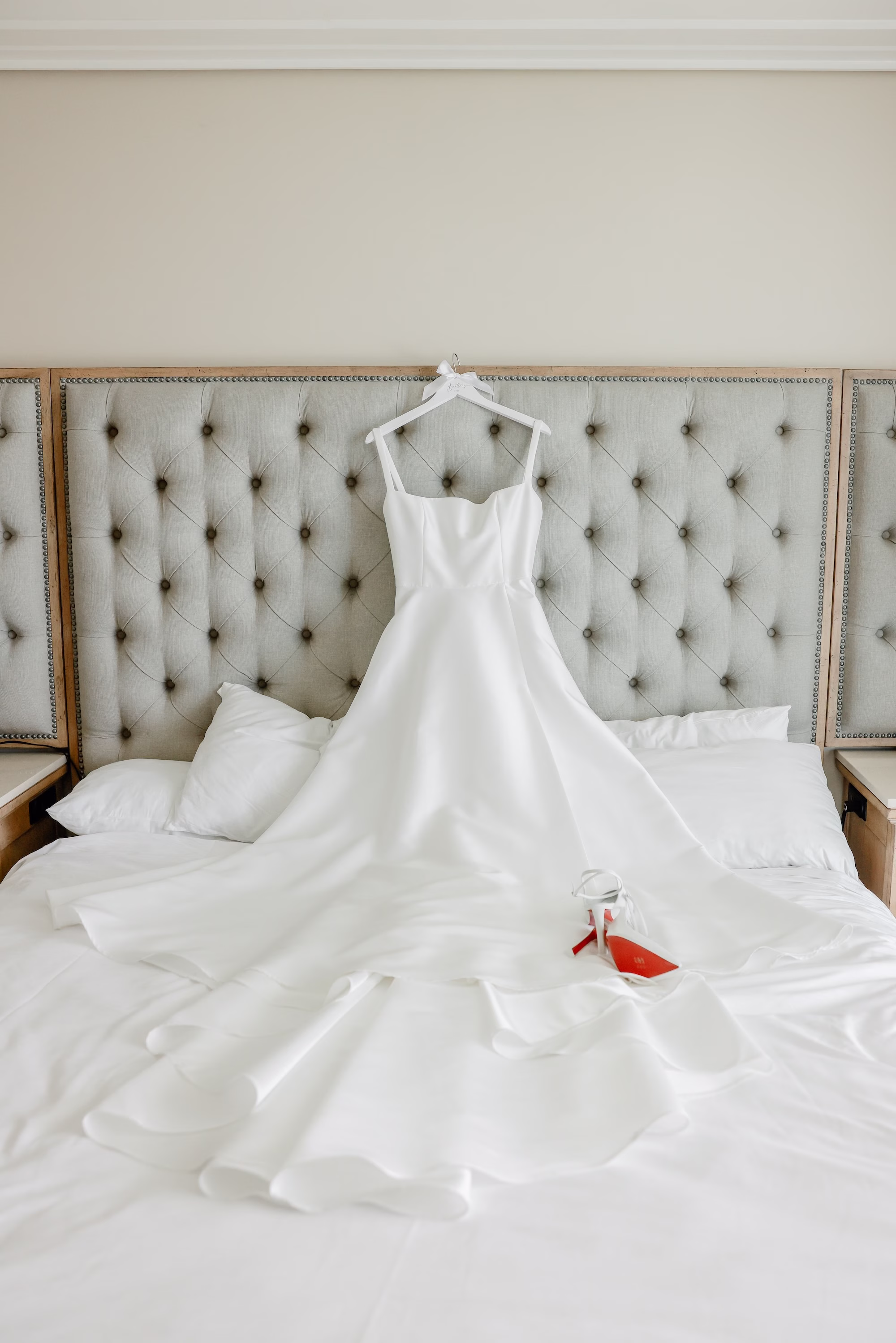 4Elegant Light Blue Coastal Florida Wedding Ideas - Elegant Blue Modern Coastal Wedding | Opal Sands Clearwater Beach Ivory Satin Strapless Ballgown Wedding Dress Hanging on Tufted Headboard with Red Sole Wedding Shoes