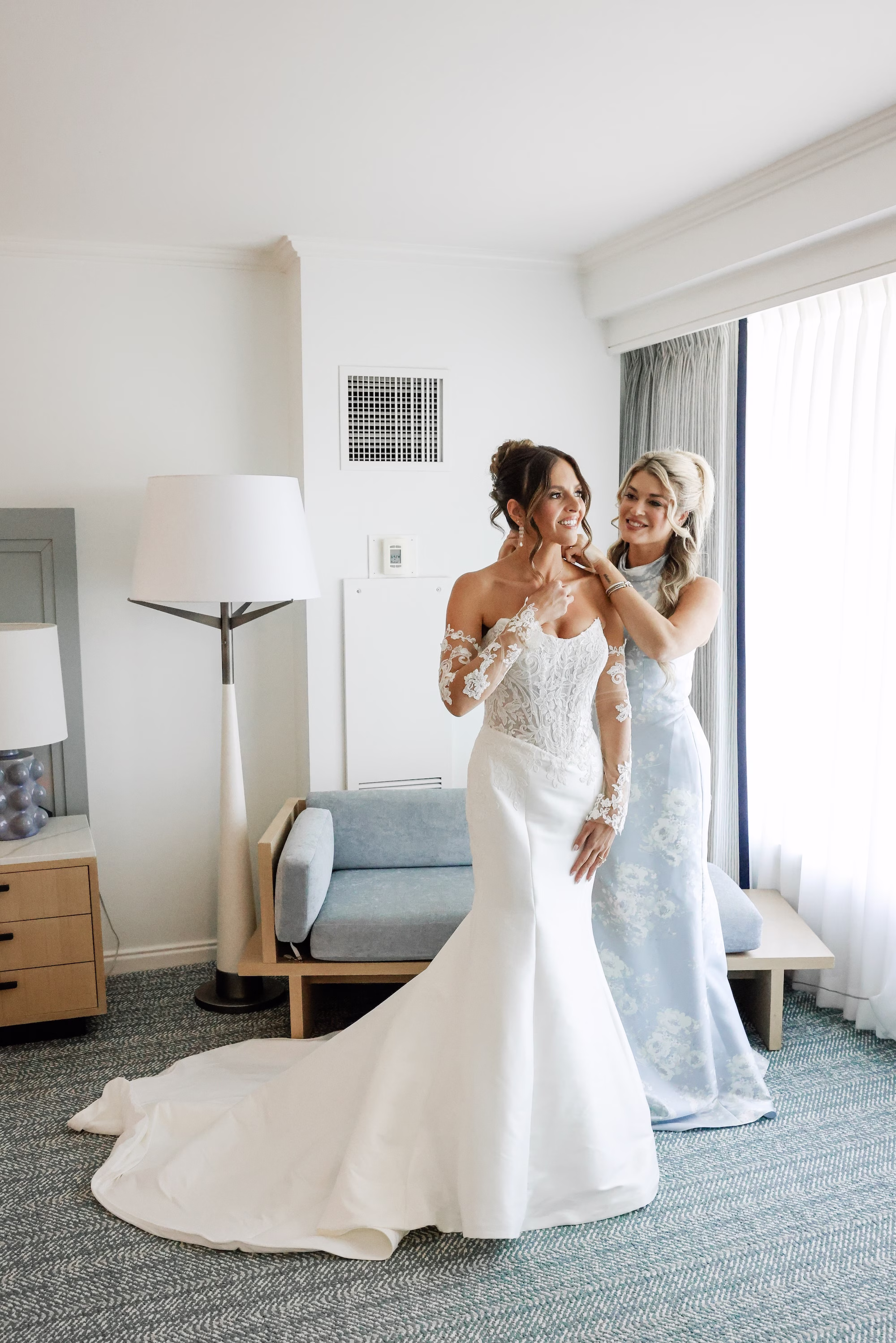 Bride and Bridesmaid Getting Ready Wedding Portrait | Floral Light Blue and White Bridesmaid Dress Inspiration | Strapless The Dessy Group White Wedding Gown with Lace Bodice and Sleeves Ideas | Soft Curled Bun Bridal Hair with Traditional Veil Inspiration | Clearwater Photographer Lifelong Photography Studio | Tampa Boutique Truly Forever Bridal | Ybor Hair and Makeup Artist Adore Bridal Hair and Makeup | Content Creator Behind The Vows