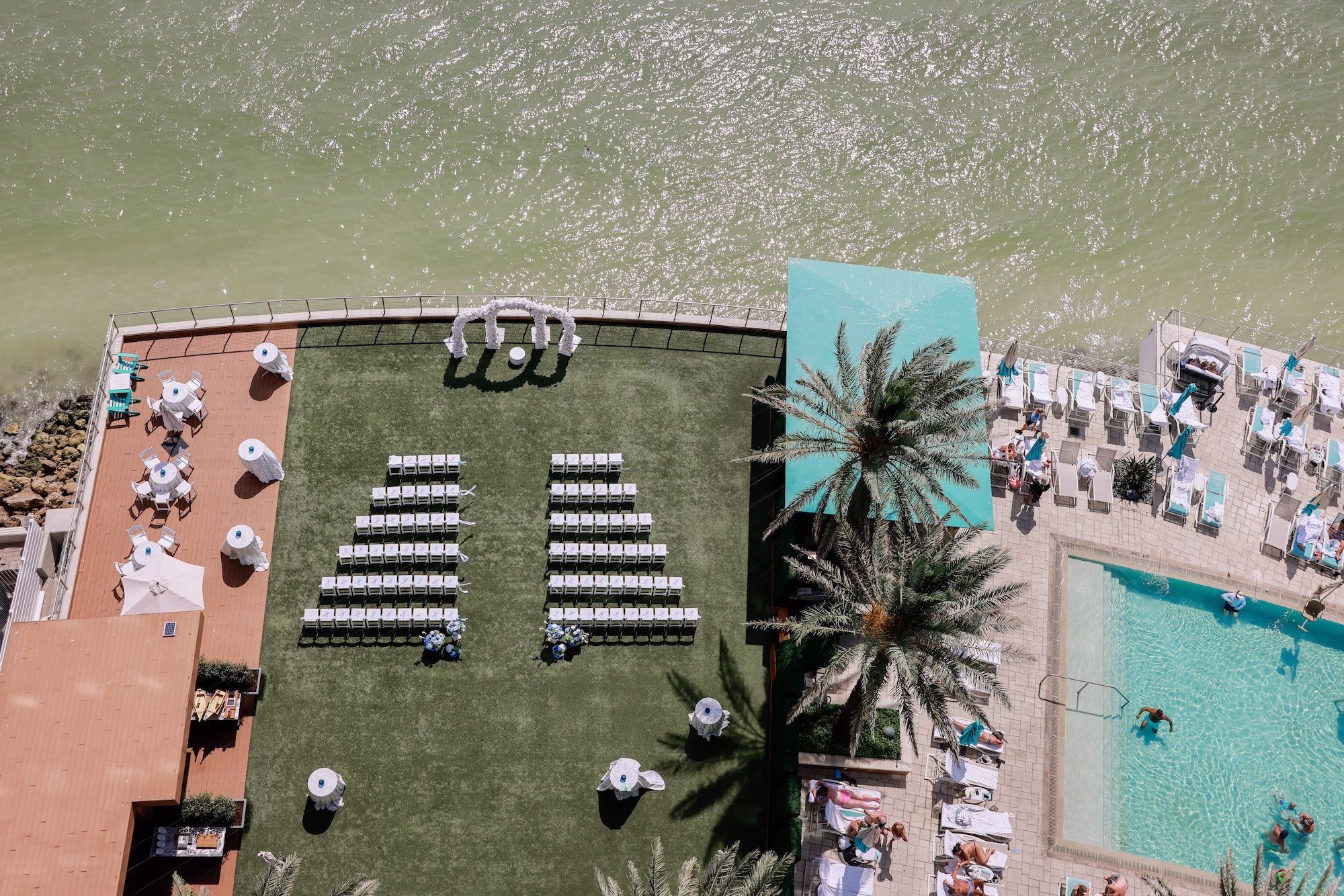 9Elegant Light Blue Coastal Florida Wedding Ideas Clearwater Venue Opal Sands - Elegant Blue Modern Coastal Wedding | Opal Sands Clearwater Beach Aerial Drone View of Rooftop Lawn Beach Wedding Ceremony Setup with White Folding Chairs, Floral Arch and Resort Pool | Rooftop Lawn Wedding Ceremony at Clearwater Beach Venue Opal Sands Resort | Photography Lifelong Photography Studio