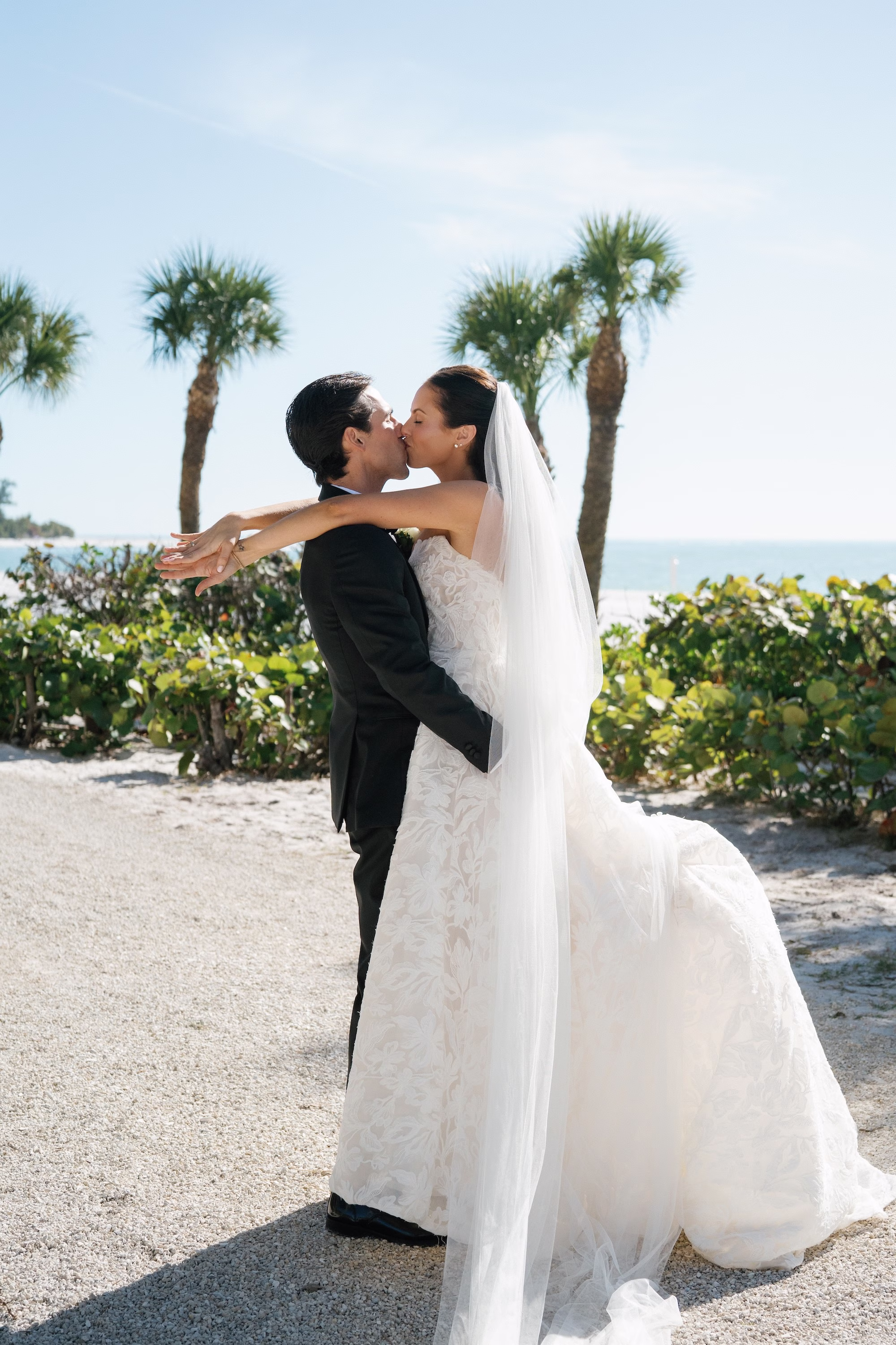 12Coastal Nancy Meyers Inspired Florida Beach Wedding - Coastal Blue, White, and Green Sarasota Wedding | The Resort at Longboat Key Club Groom Lifting and Kissing Bride Wedding Portrait with Palm Trees and Gulf of Mexico Behind Them
