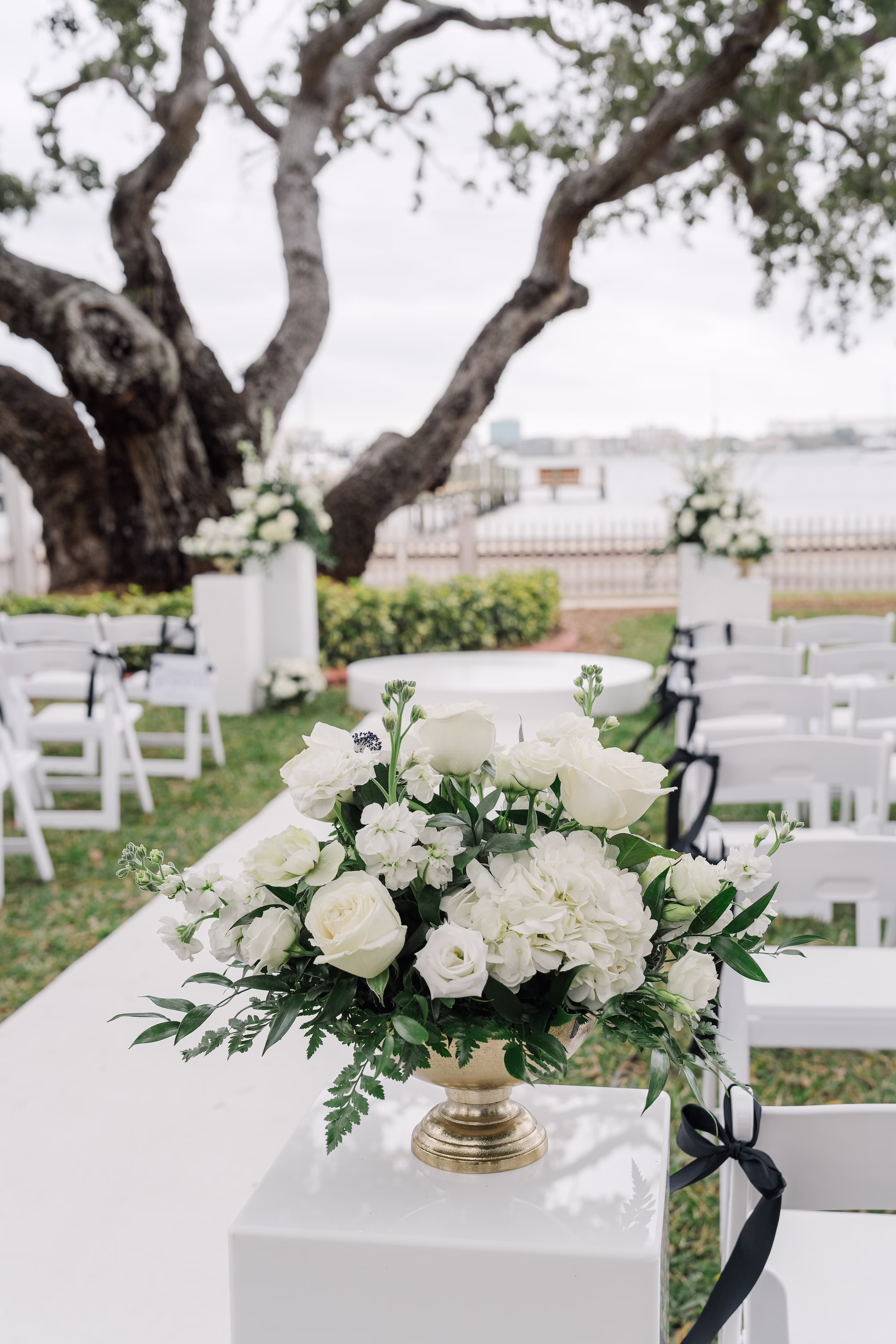 White Rose and Greenery Aisle Arrangement on White Pedestal with White Folding Chairs and Black Ribbon Wedding Ceremony Decor Ideas