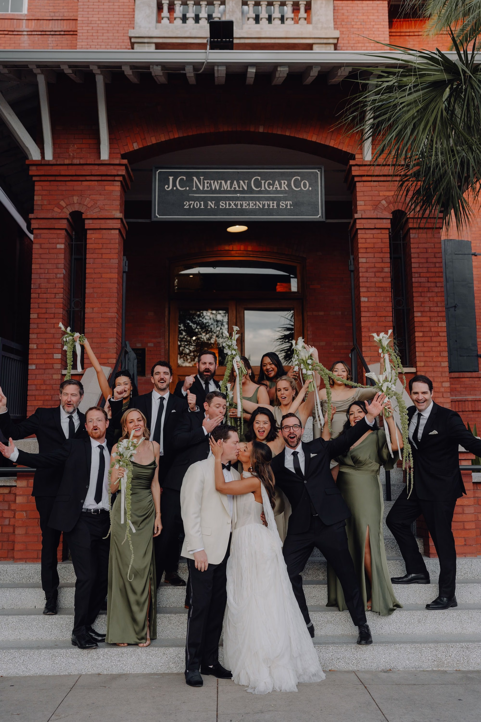 15Classic Modern Black and White Wedding Ideas - Modern Black and Ivory Ybor City Wedding | J.C. Newman Cigar Co. Wedding Party Portrait in Black Tuxedos and Sage Green Bridesmaid Dresses on Front Steps of Historic Ybor City Cigar Factory | Tampa Venue J.C. Newman Cigar Co.