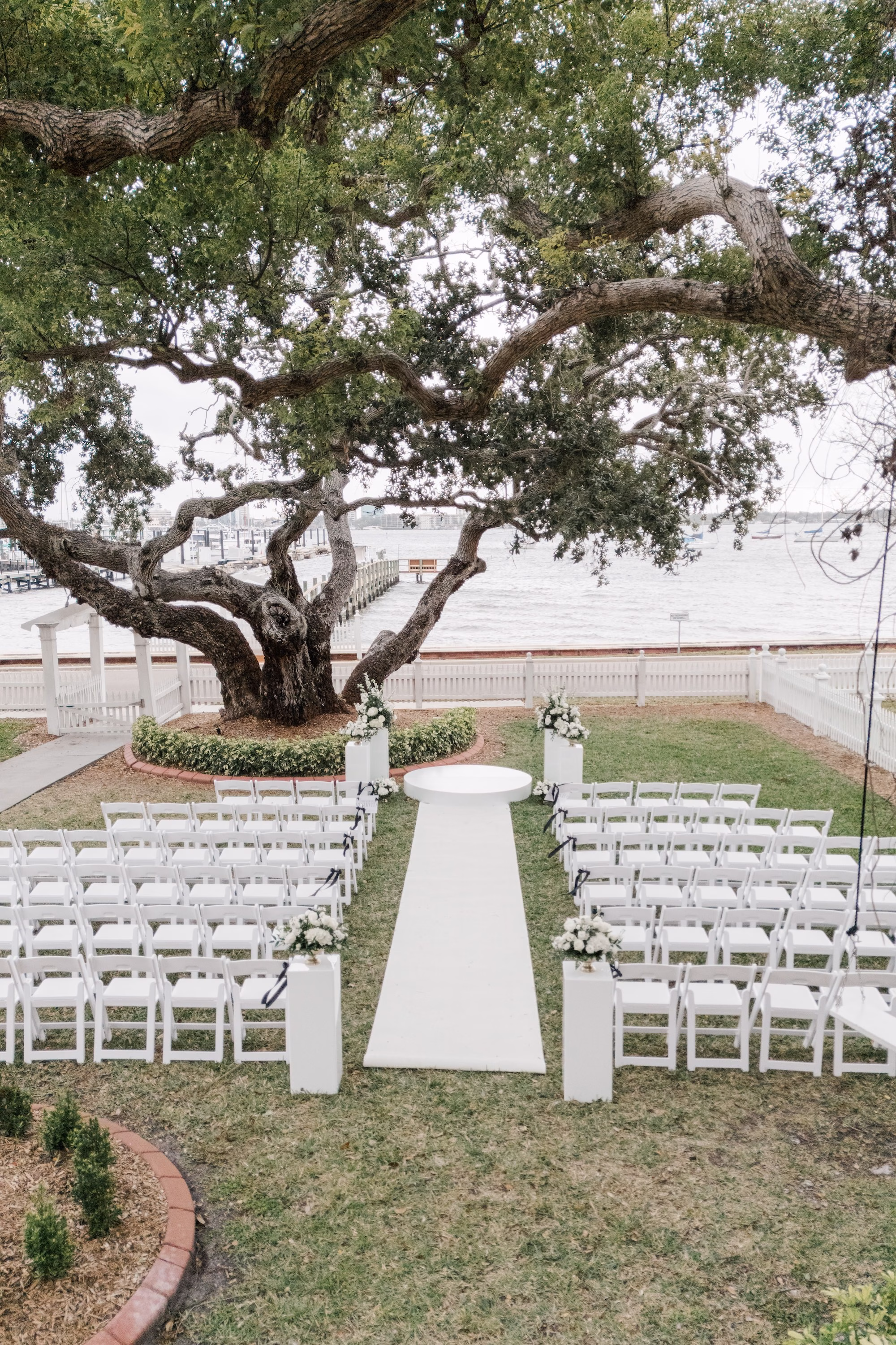 Waterfront Old Florida Wedding Ceremony Under Live Oak with White Aisle Runner, White Chairs and Round Ceremony Platform Ideas | Palmetto Venue Palmetto Riverside Bed and Breakfast | Rentals Kate Ryan Event Rentals