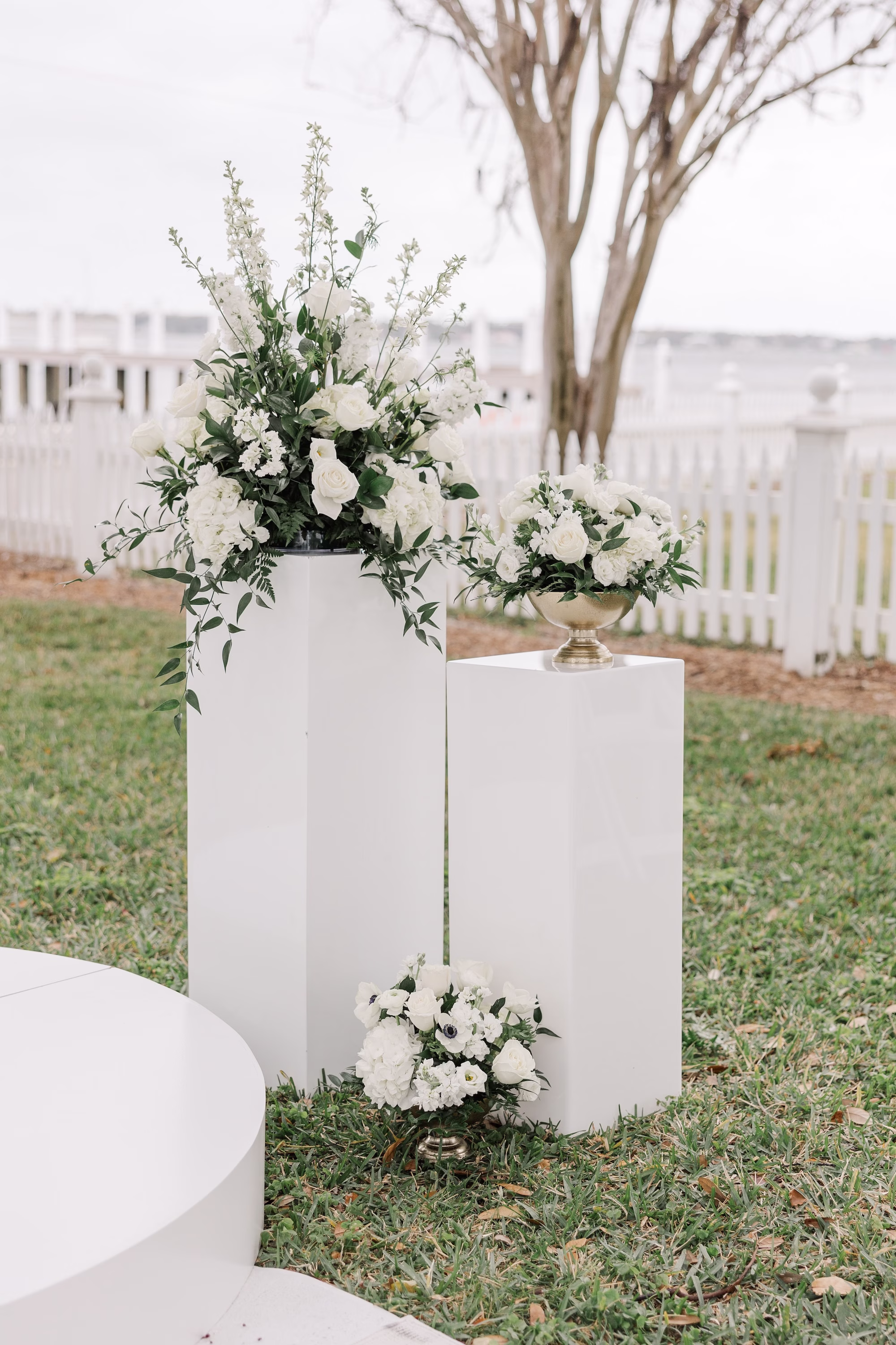 White Pedestal Wedding Ceremony Altar Arrangements with White Roses, Hydrangea and Greenery Beside Round White Platform Ideas | Palmetto Rentals Kate Ryan Event Rentals