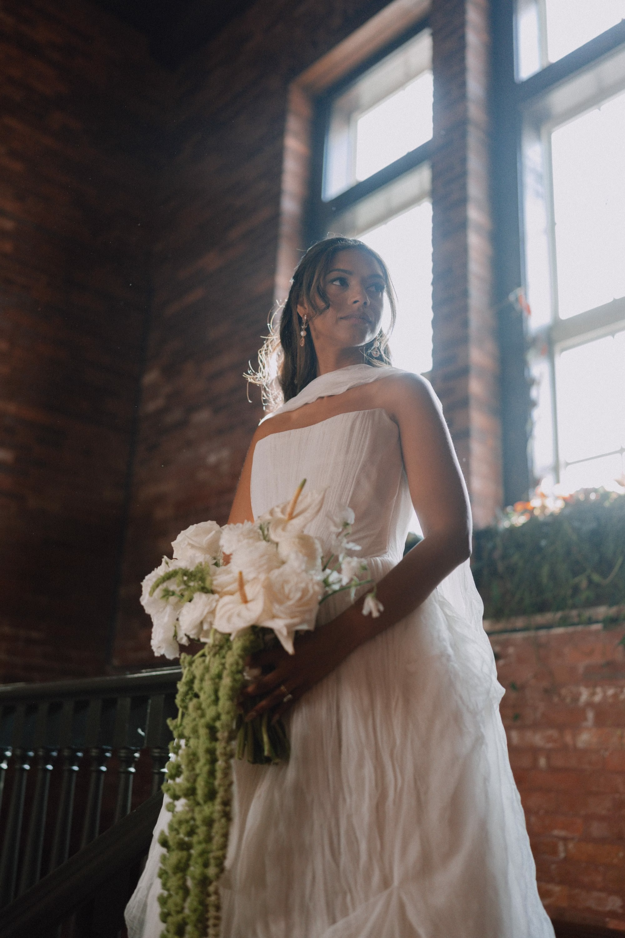 18Classic Modern Black and White Wedding Ideas - Modern Black and Ivory Ybor City Wedding | J.C. Newman Cigar Co. Bridal Portrait in Ivory Strapless Watters Wedding Dress with Neck Scarf Holding White Anthurium and Hanging Amaranthus Bouquet Against Red Brick