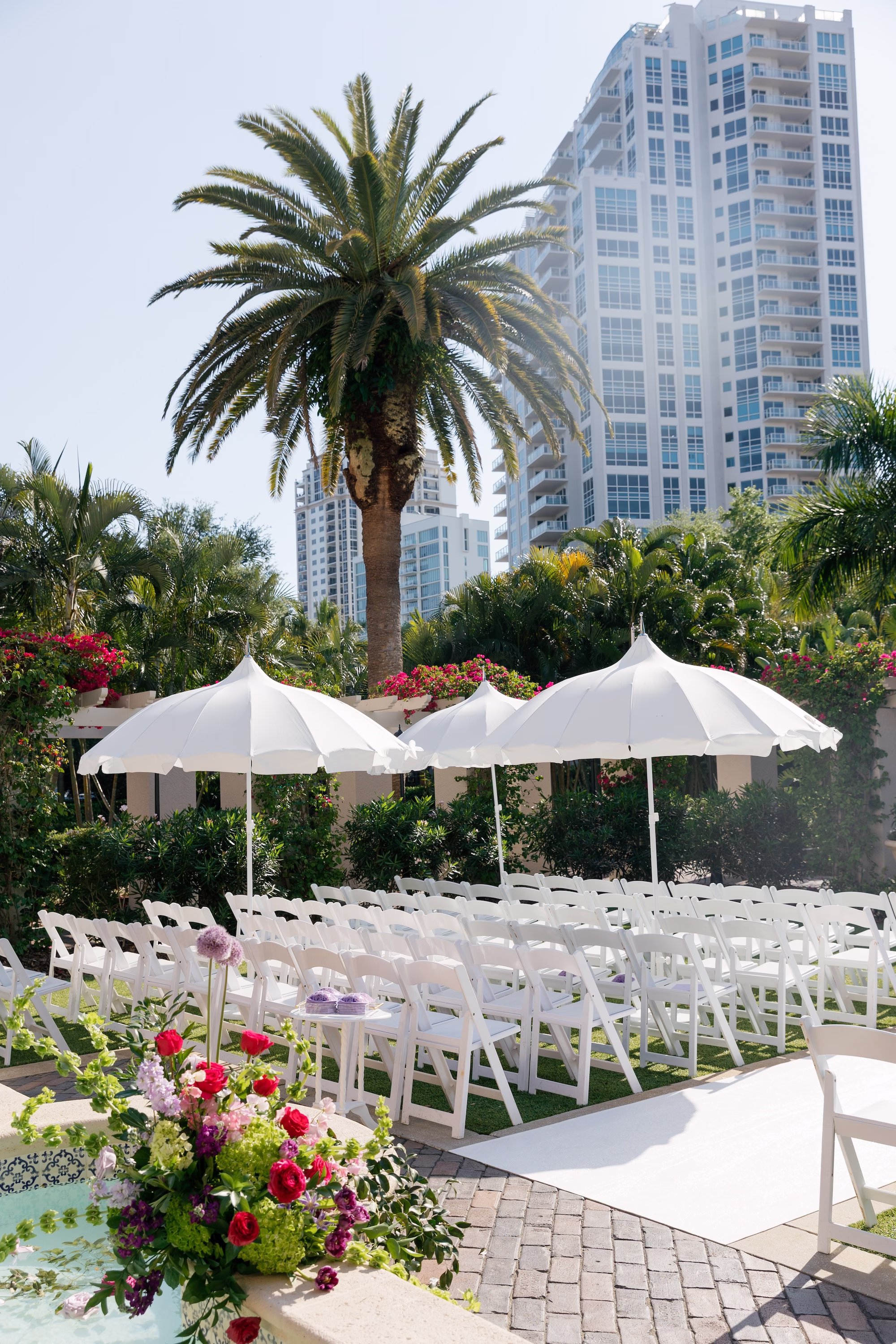 Outdoor Garden Wedding Ceremony with White Folding Chairs, White Fringe Umbrellas and Pink and Purple Aisle Floral Arrangements Ideas | Tea Garden Wedding Ceremony at St. Pete Venue The Vinoy | Planner Parties A' La Carte | Florist Bruce Wayne Florals