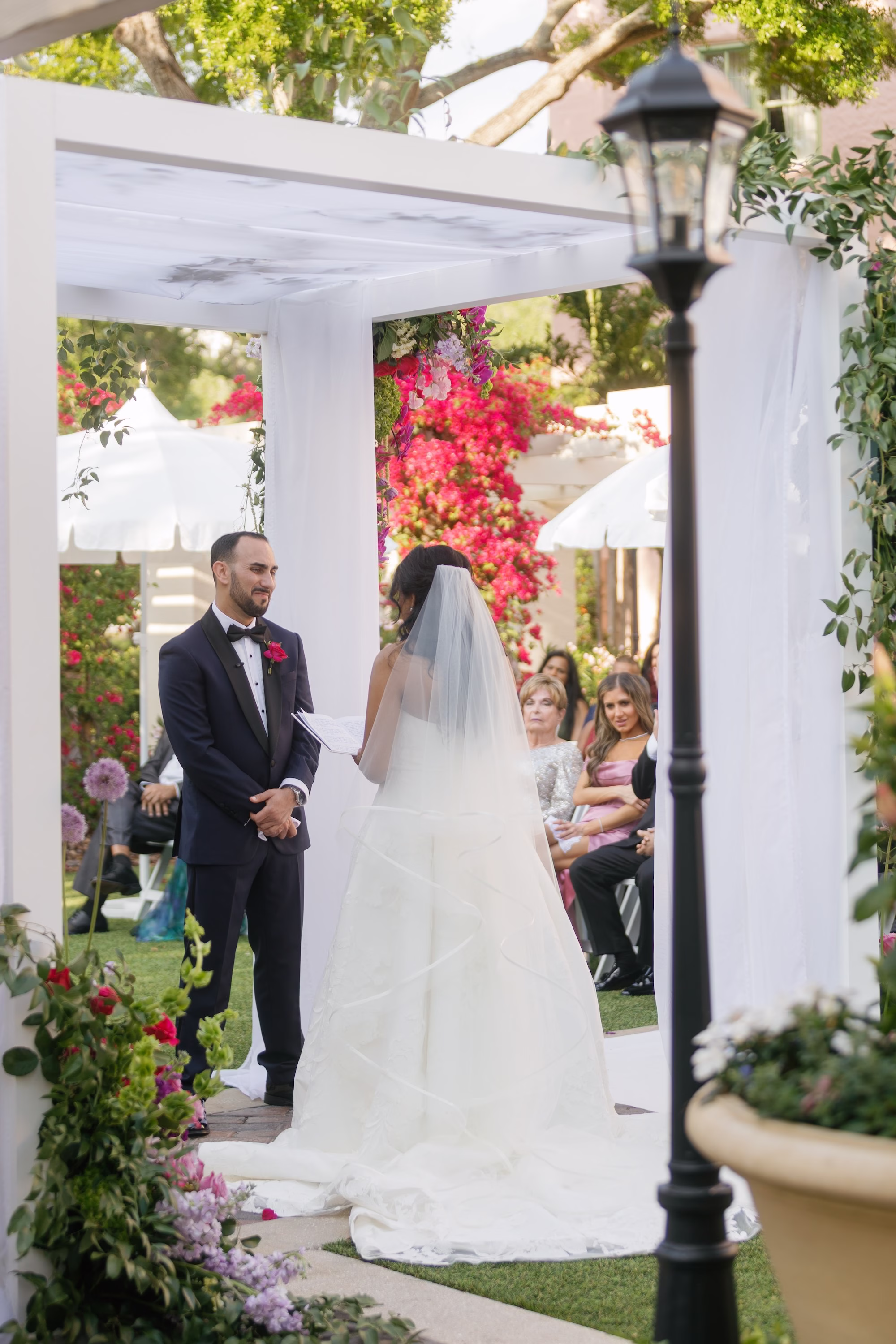 Groom's Reaction to Bride Walking Down Wedding Ceremony Aisle Under Floral Chuppah