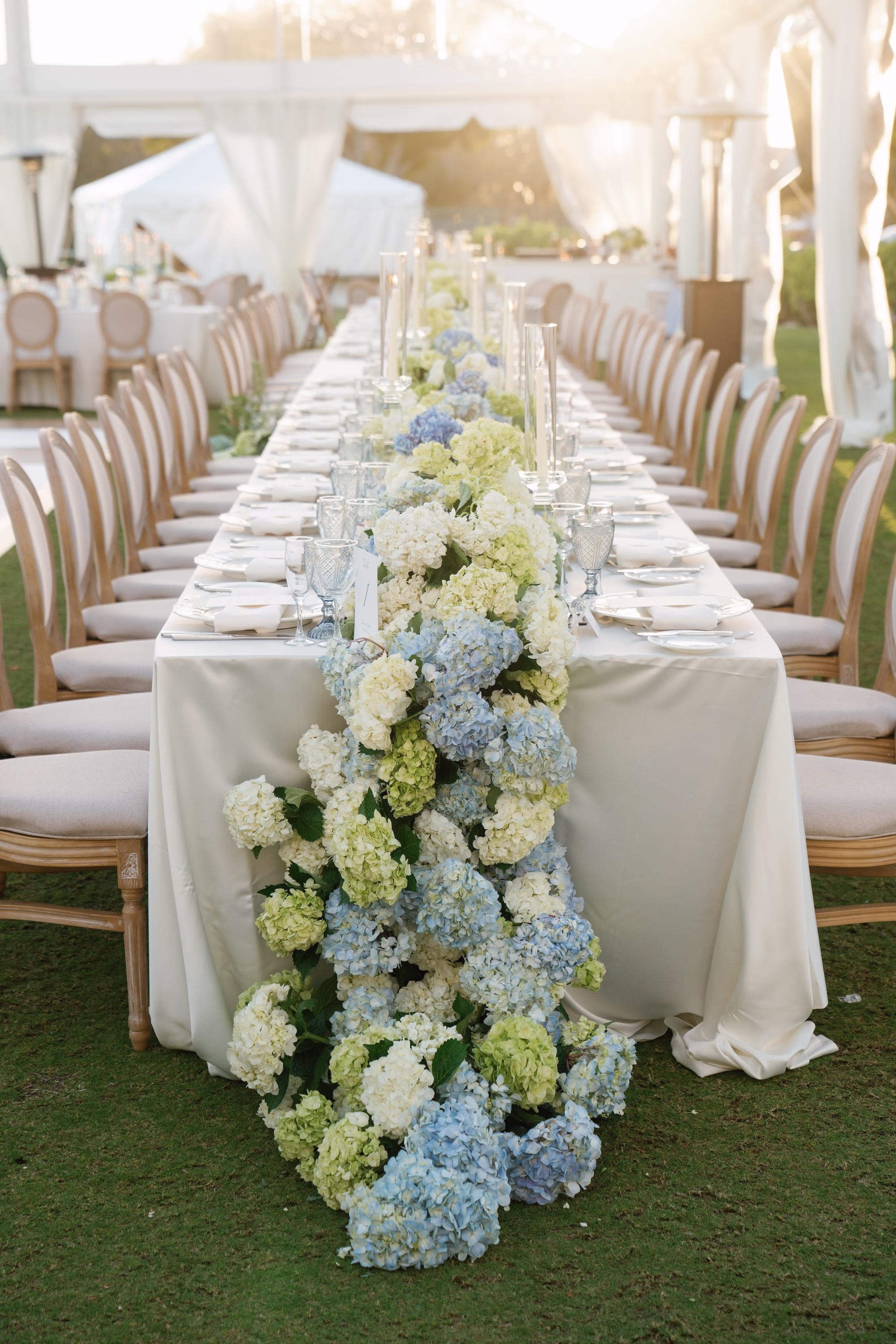 29Coastal Nancy Meyers Inspired Florida Beach Wedding - Coastal Blue, White, and Green Sarasota Wedding | The Resort at Longboat Key Club Long Head Table with Blue, White and Green Hydrangea Floral Runner, Louis Chairs and Champagne Linens Under Clear Tent Wedding Reception Ideas