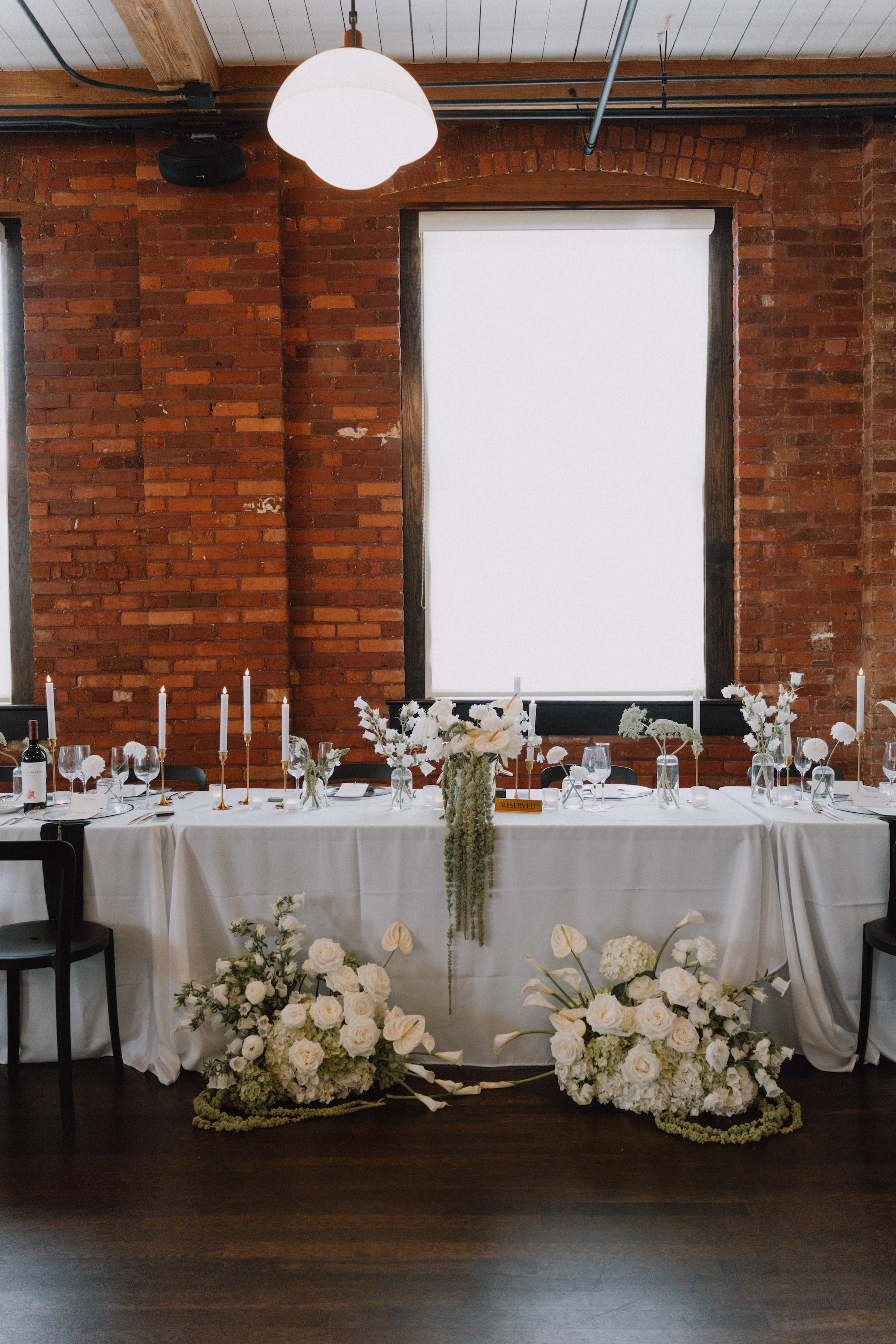 30Classic Modern Black and White Wedding Ideas Tampa Venue JC Newman Cigar Co - Modern Black and Ivory Ybor City Wedding | J.C. Newman Cigar Co. White Head Table with Ground Floral Arrangements of White Roses and Hanging Amaranthus Against Exposed Brick Wedding Reception Sweetheart Table Decor Ideas | Wedding Reception at Tampa Venue J.C. Newman Cigar Co.