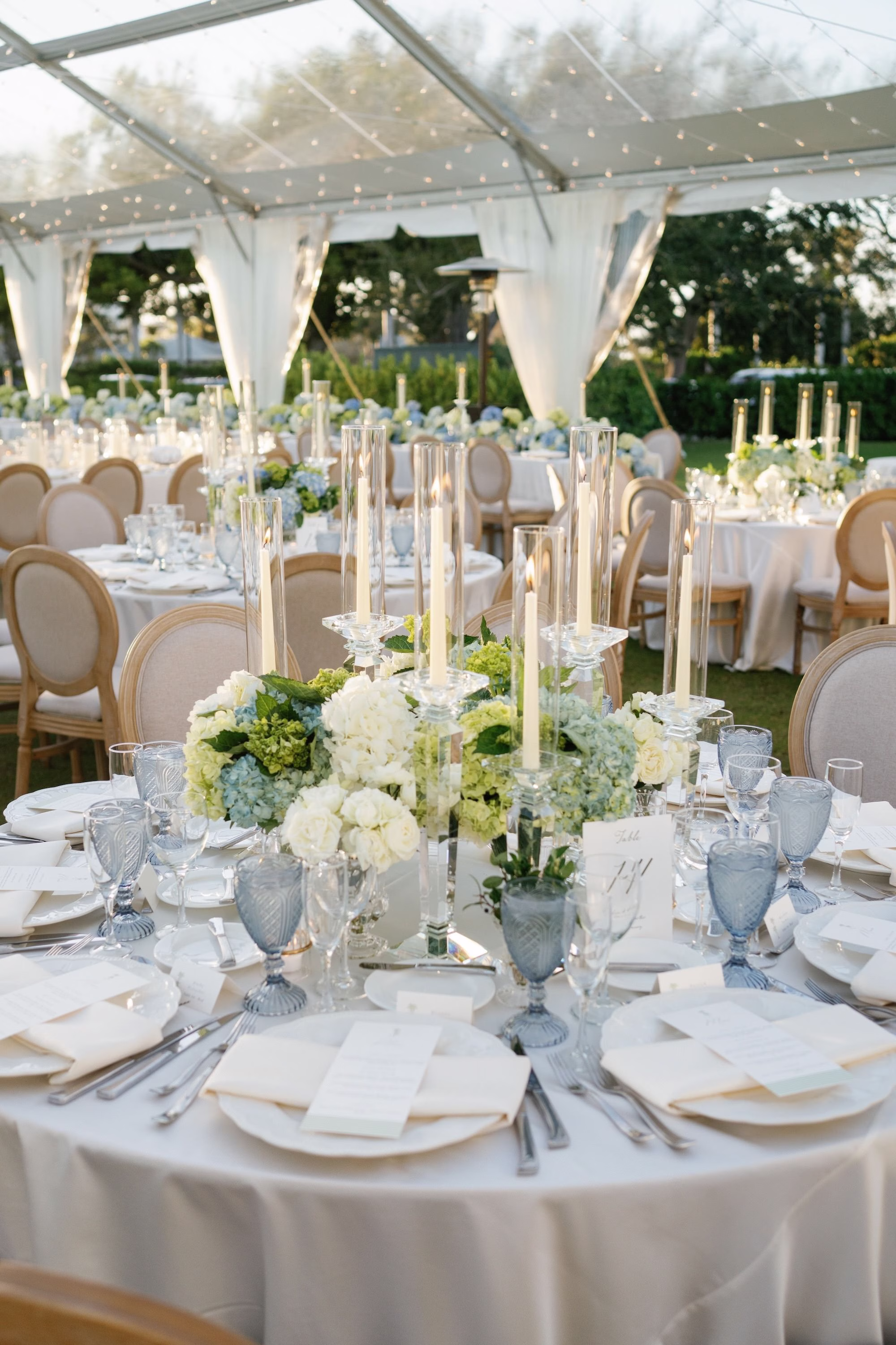 31Coastal Nancy Meyers Inspired Florida Beach Wedding - Coastal Blue, White, and Green Sarasota Wedding | The Resort at Longboat Key Club Coastal Blue and White Wedding Reception Tablescape with Taper Candles, Hydrangea Centerpieces and Blue Cut Glass Goblets Under Clear Tent Ideas | Tented Lawn Wedding Reception