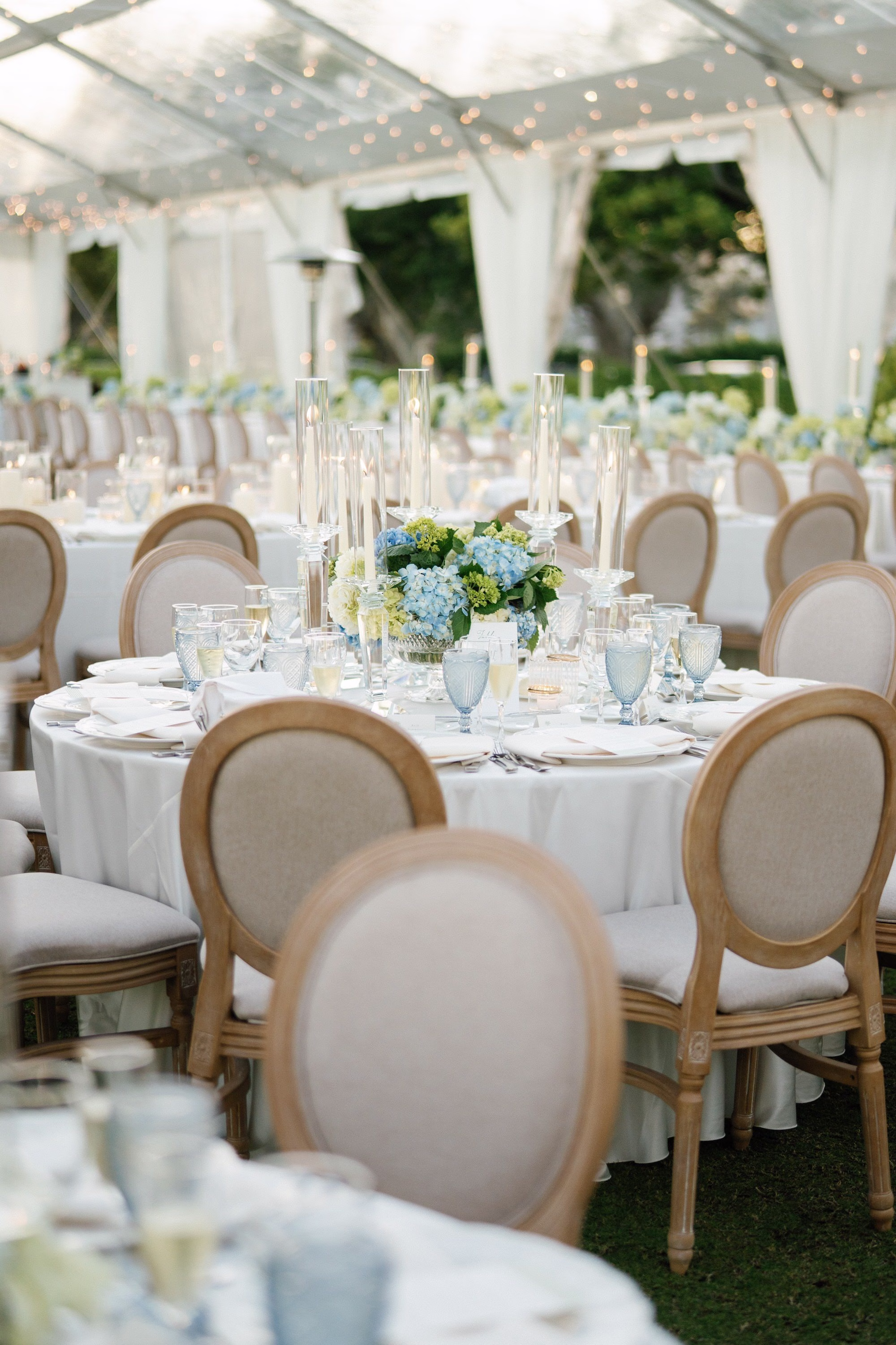 32Coastal Nancy Meyers Inspired Florida Beach Wedding - Coastal Blue, White, and Green Sarasota Wedding | The Resort at Longboat Key Club Round Wedding Reception Tables with Louis Chairs, Ivory Linens and Blue and White Hydrangea Centerpieces Under Clear Tent Ideas | Tented Lawn Wedding Reception