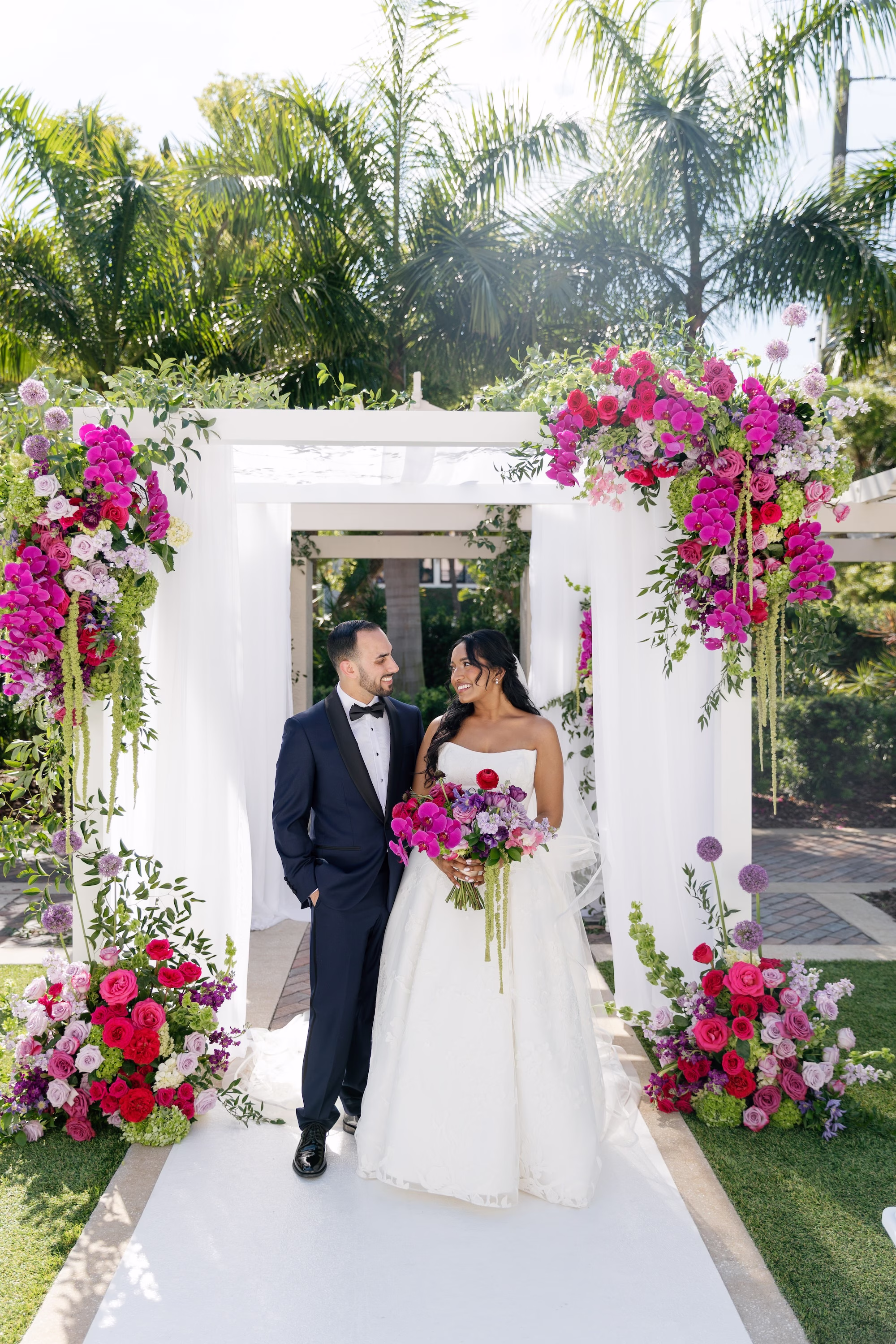 Bride and Groom Wedding Ceremony Portrait Under White Draped Chuppah with Cascading Fuchsia Orchids and Pink Bougainvillea | St. Pete Florist Bruce Wayne Florals | Planner Parties A' La Carte
