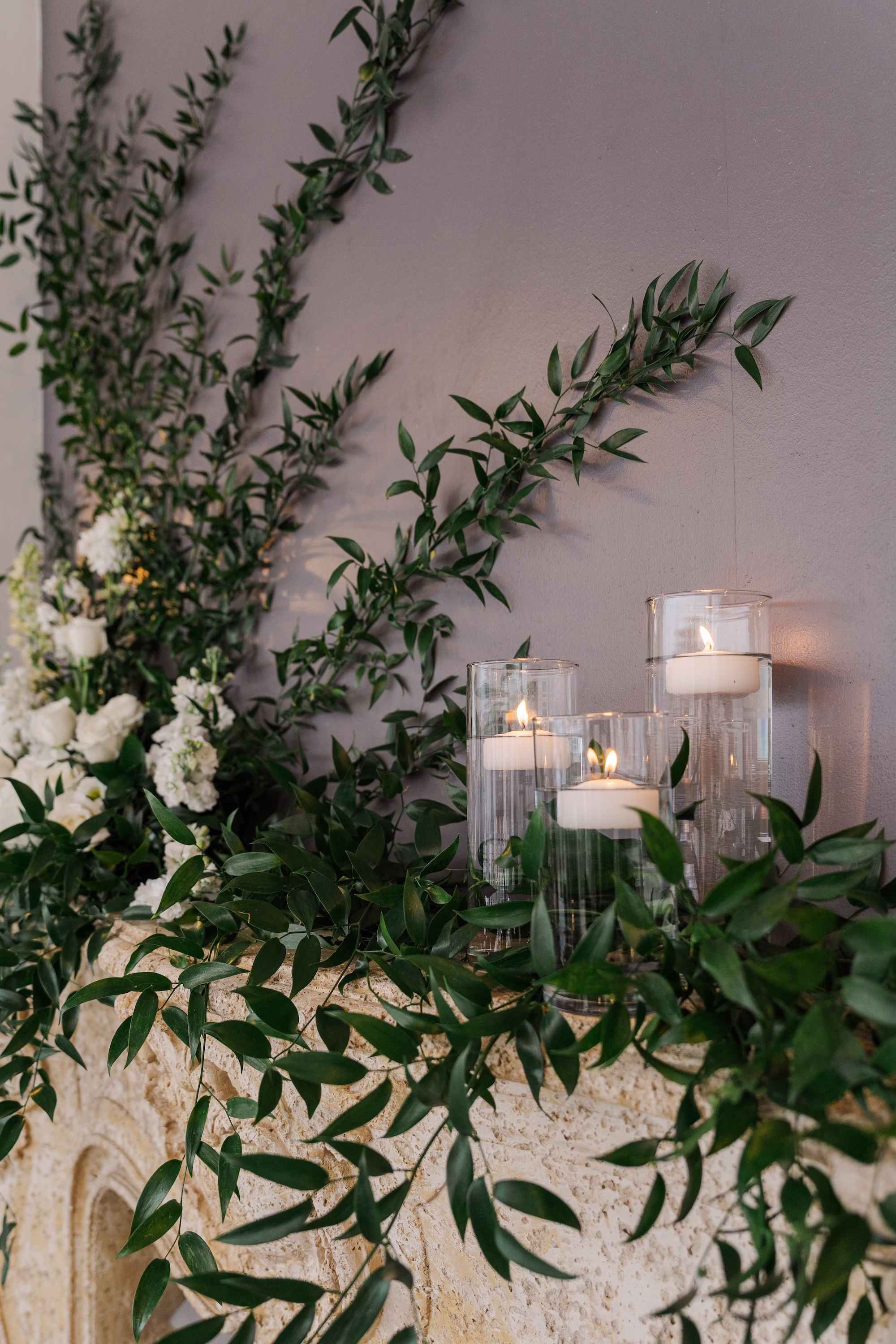 White Rose and Italian Ruscus Greenery Fireplace Mantel Installation with Pillar Candles Wedding Decor Ideas