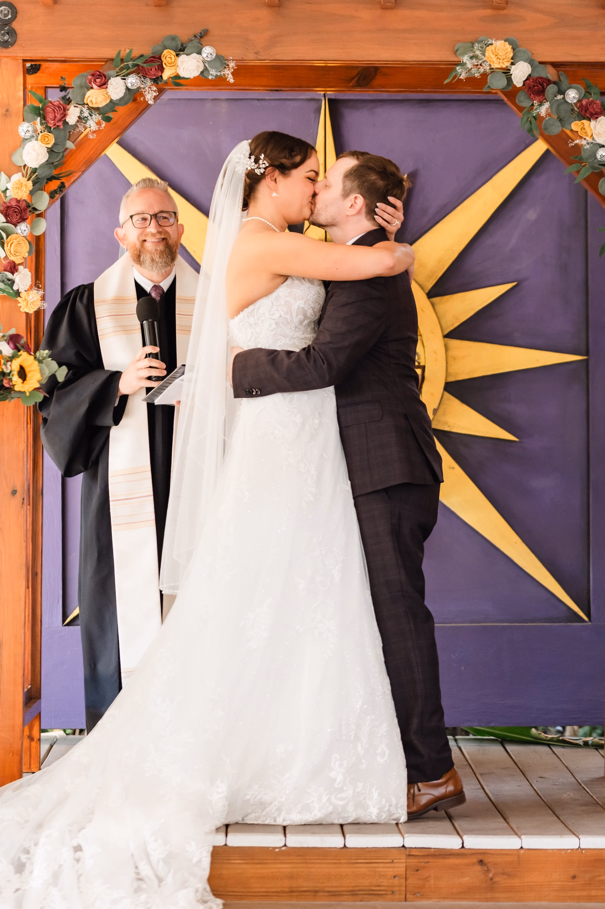 11St Pete Museum Outdoor Garden Ceremony Venue Duncan McClellan Gallery - Neon Disco Meets Old Florida St. Pete Wedding | FloridaRAMA Bride and Groom First Kiss Wedding Portrait | Wooden Altar with Purple Sunburst Door Backdrop with Wooden Pergola Wedding Ceremony Decor Inspiration | White, Plum and Mustard Yellow Floral Decor Ideas