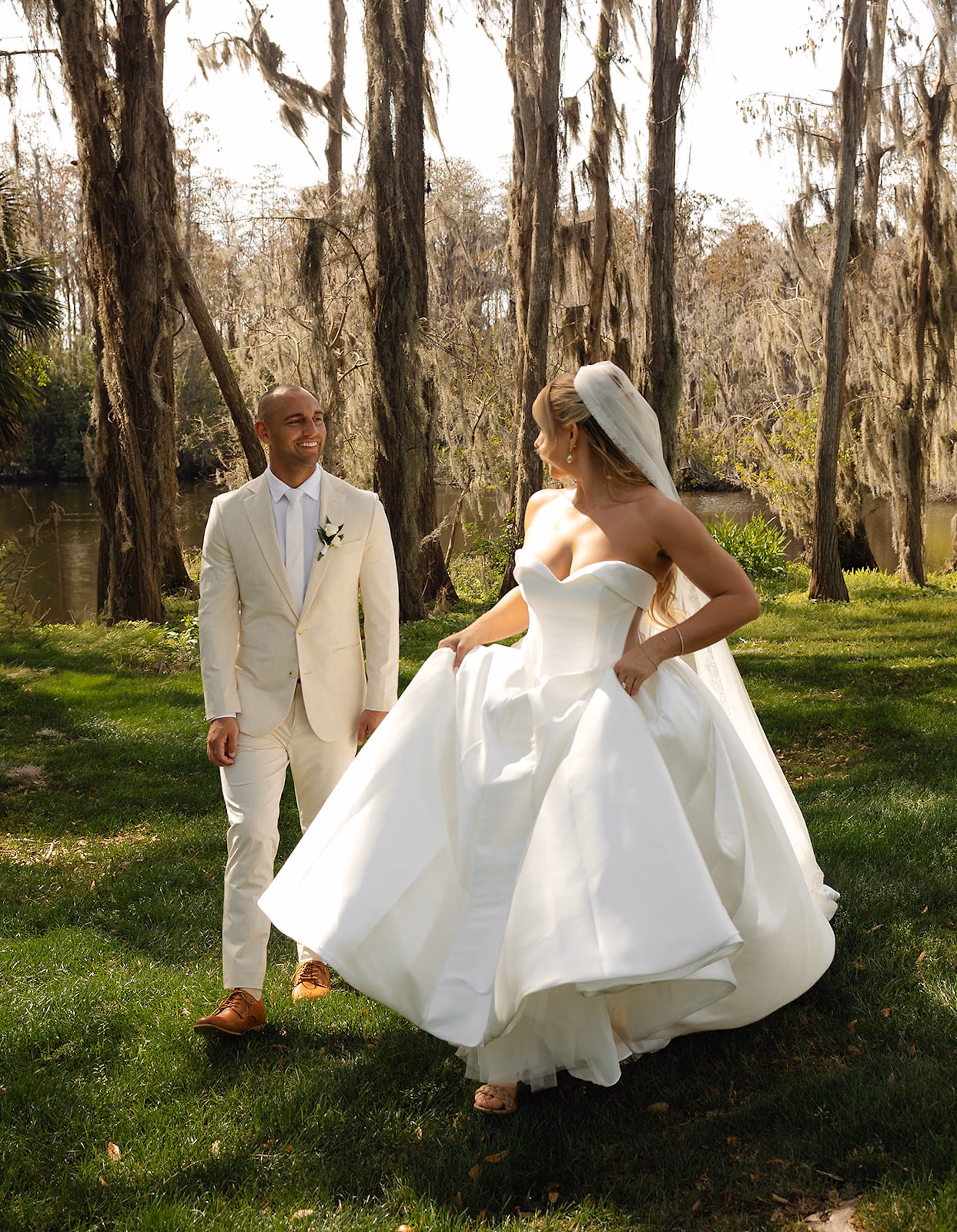 Bride Twirling Ballgown Wedding Dress with Groom in Cream Linen Suit Among Mossy Trees