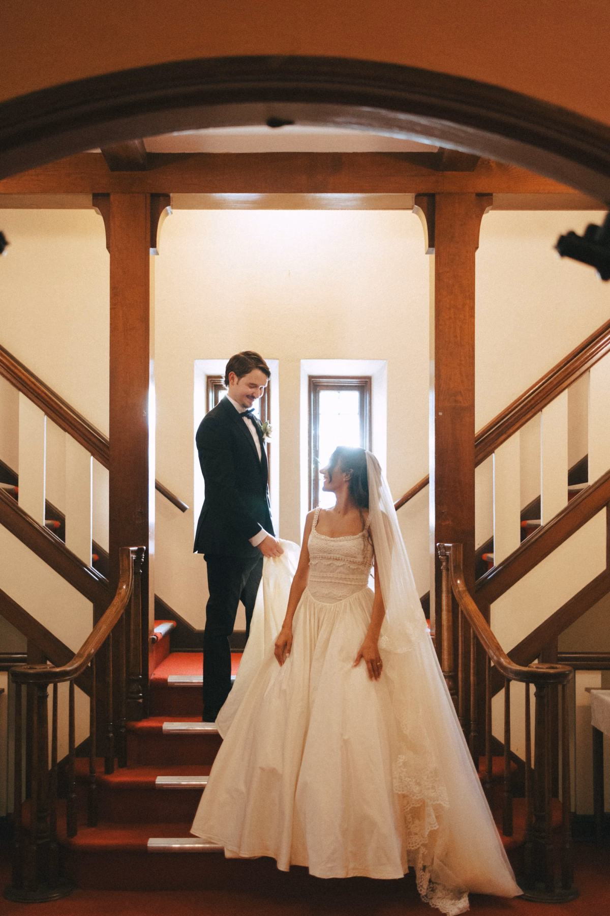 Groom in Black Tuxedo Leading Bride in Ballgown Wedding Dress Up Wooden Church Staircase | St. Pete Venue Trinity Lutheran Church