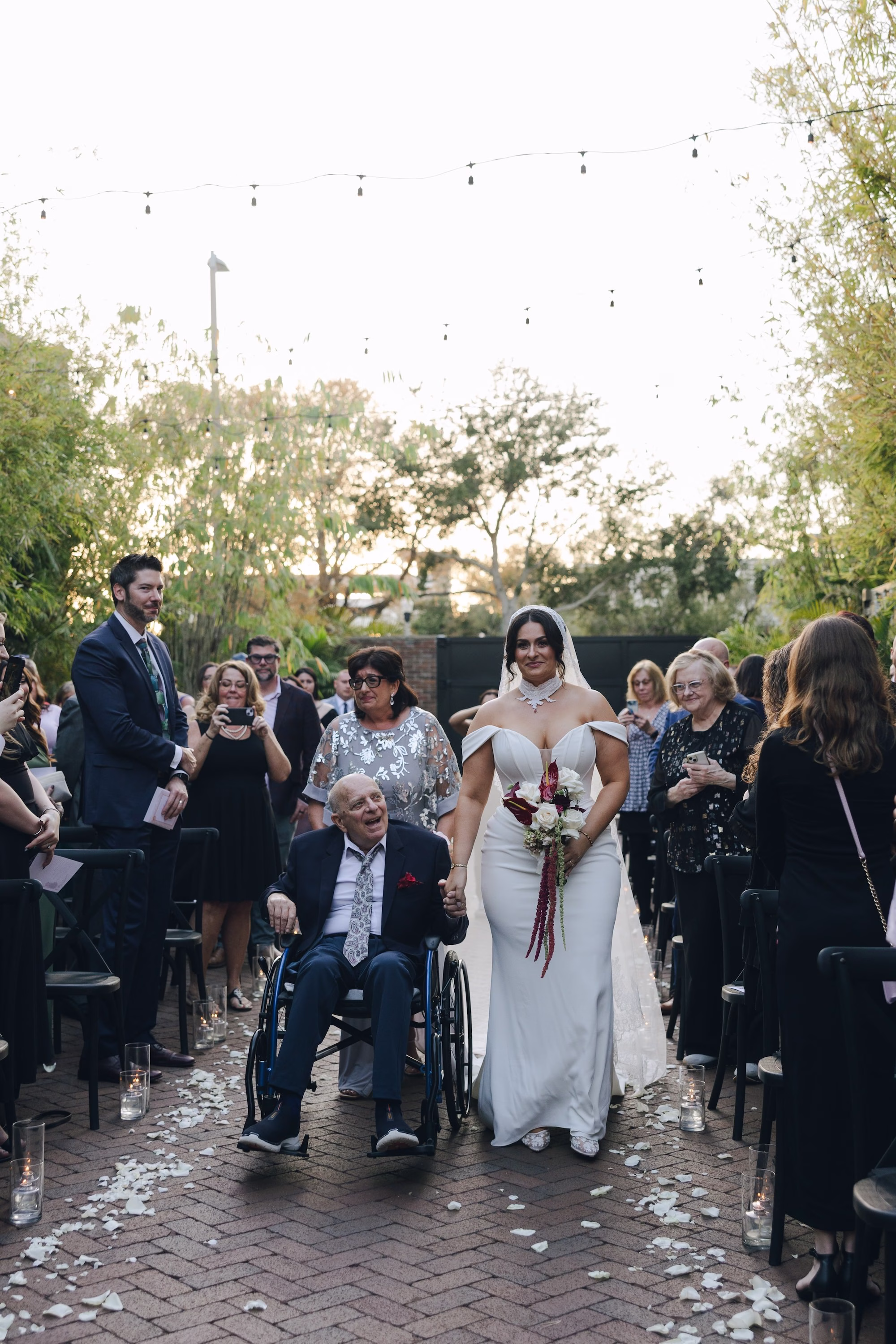 14Burgundy Vintage Romance Wedding Ideas - Vintage Romance Pink and Burgundy Downtown St. Pete Wedding | NOVA 535 Bride Walking Down Petal-Lined Brick Aisle with Father in Wheelchair at Bamboo Courtyard Wedding Ceremony