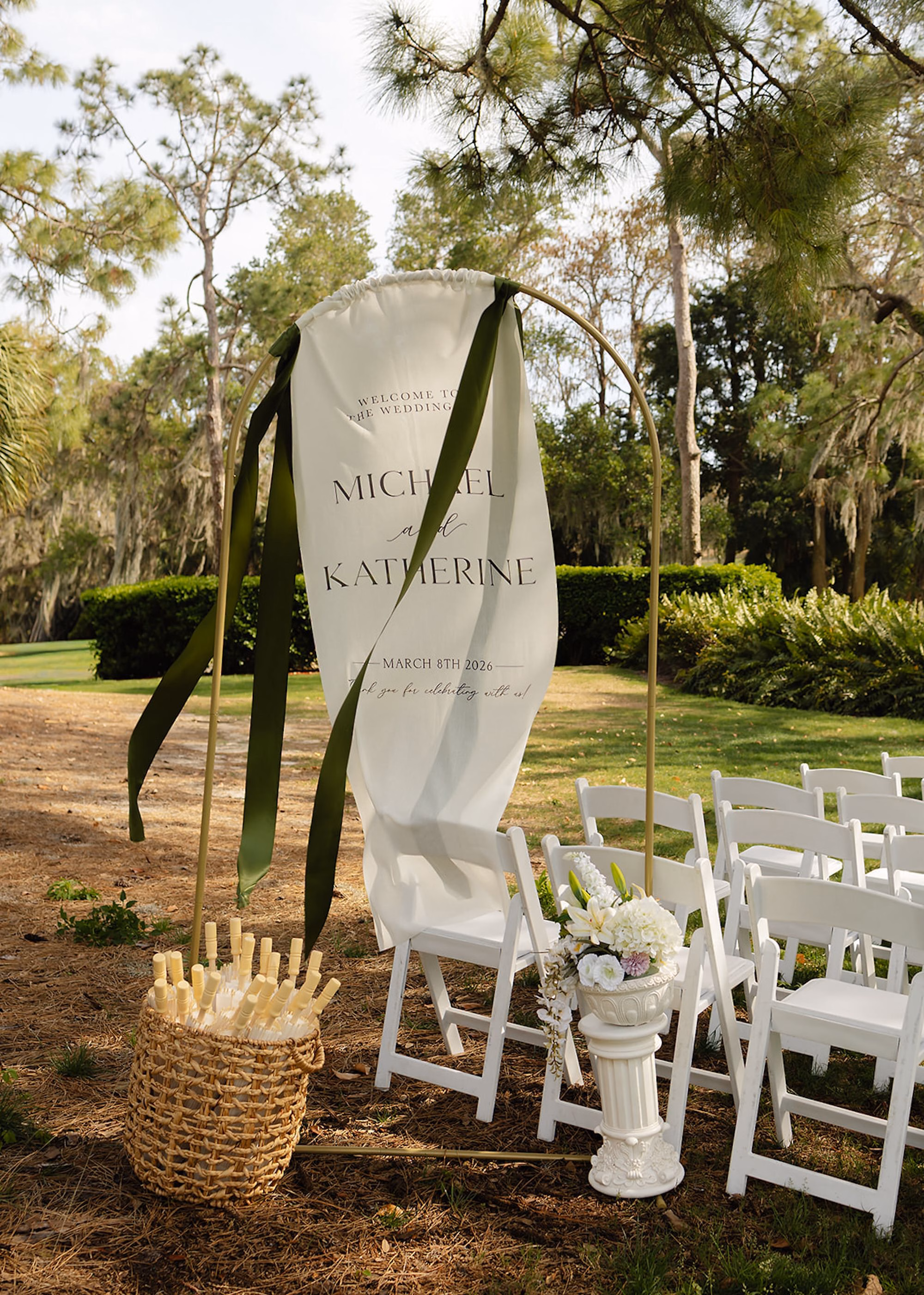 Draped Fabric Wedding Welcome Sign with Olive Ribbon, Woven Basket of Fans and White Folding Chairs at Outdoor Ceremony Ideas