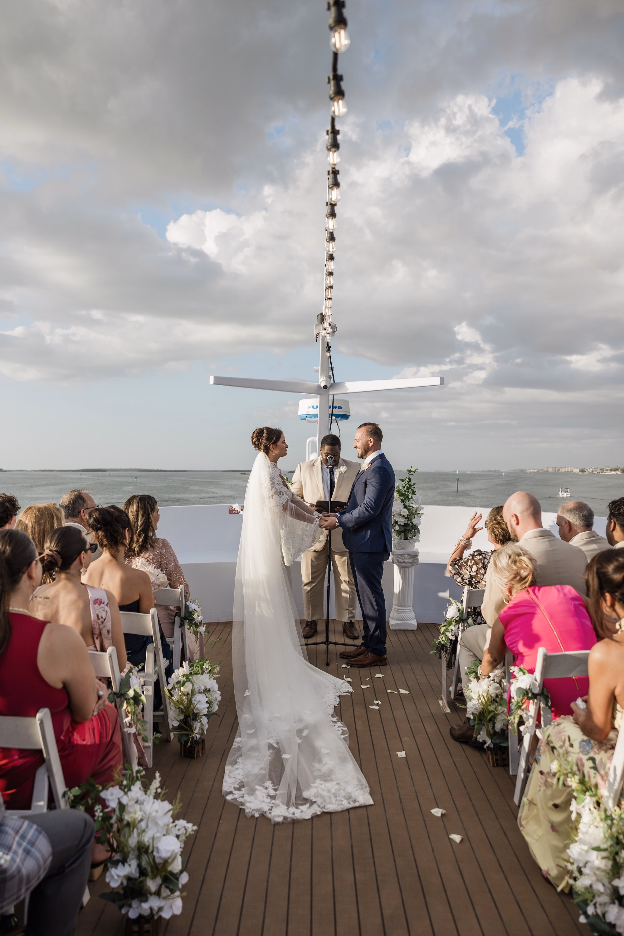 Bride and Groom Wedding Ceremony Vow Exchange Wedding Portrait | White Ceremony Folding Chairs | White Roses and Greenery Floral Arrangement Aisle Decor Inspiration | Yacht Deck Wedding Ceremony Clearwater Venue Yacht StarShip