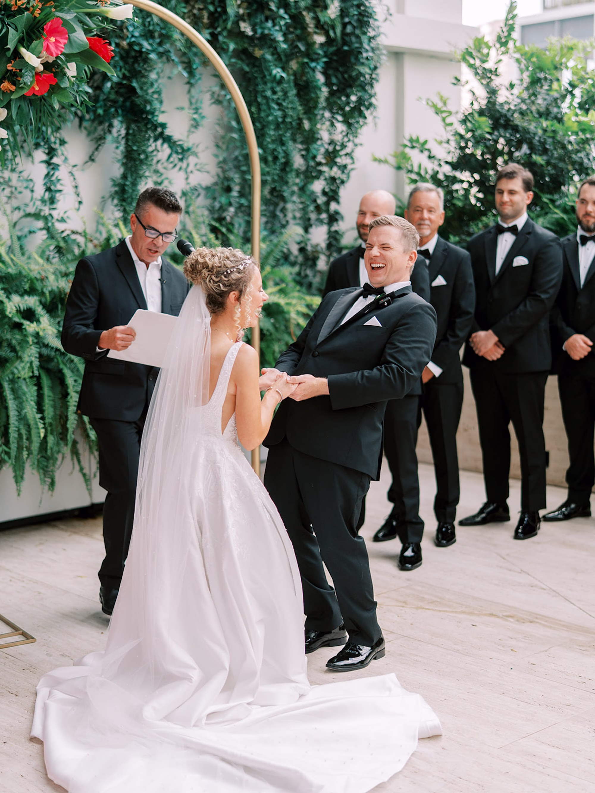 Groom Reacting as Bride Reads Vows Under Gold Arch at Rooftop Wedding Ceremony